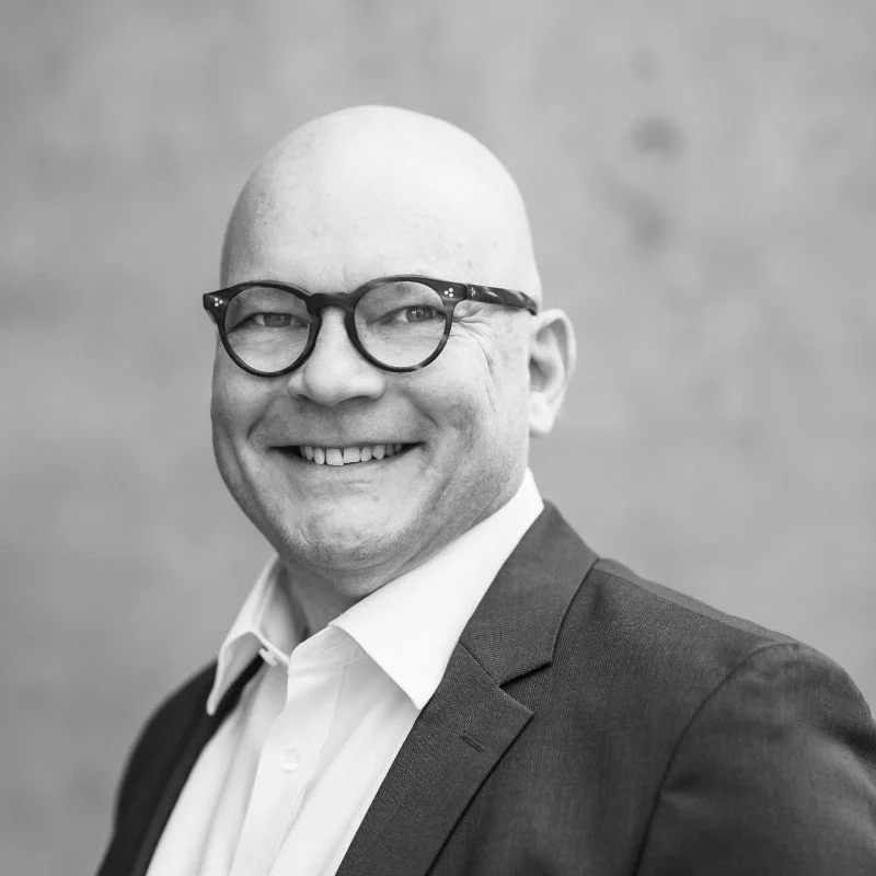Man wearing glasses and a blazer smiling at the camera.