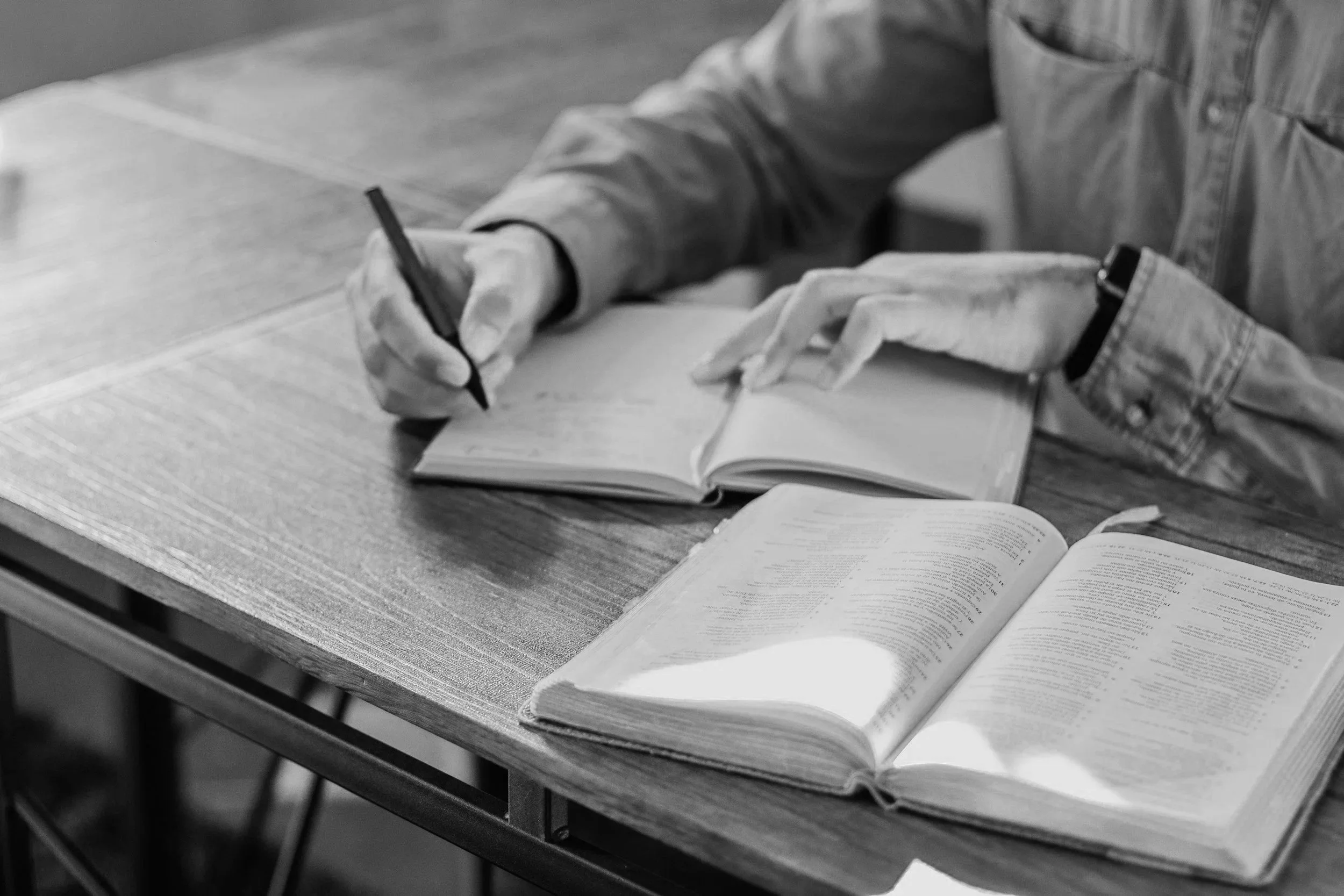 Open Bible, blank notebook, cup of coffee, red pen on dark table.