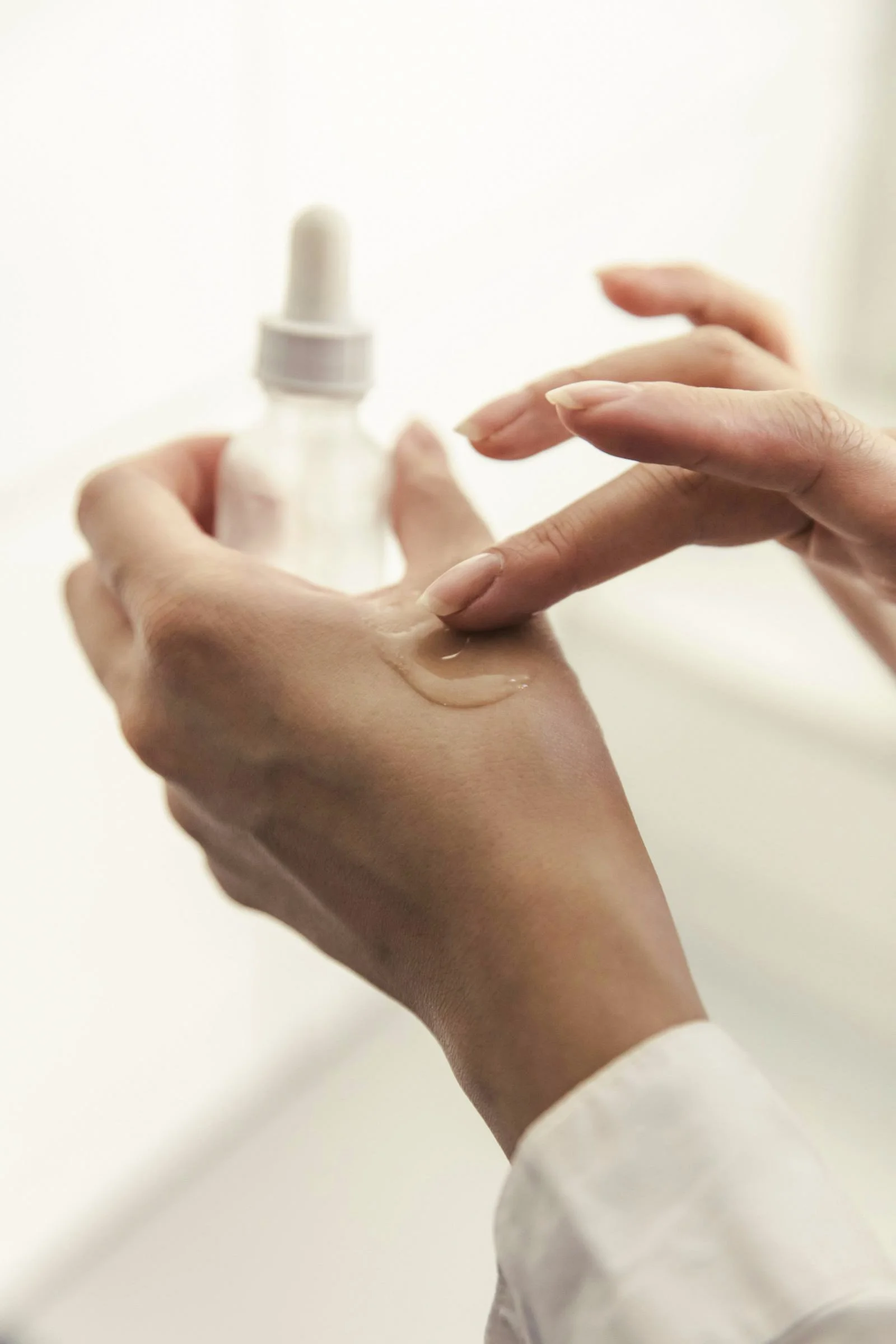 Person applying skincare serum or facial oil to their hand from a dropper bottle.