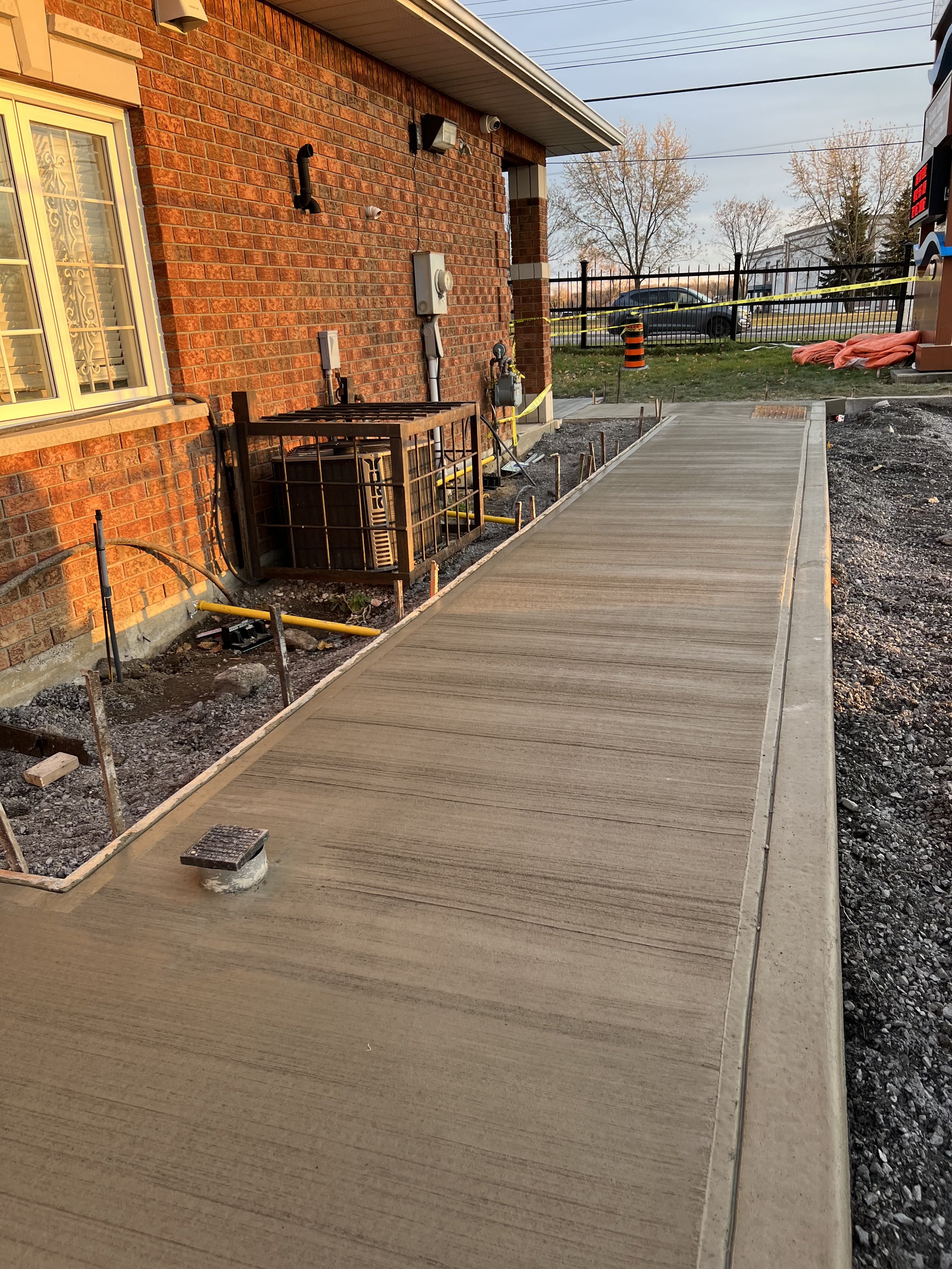 Freshly poured concrete pathway next to a brick building, with construction materials and equipment around.