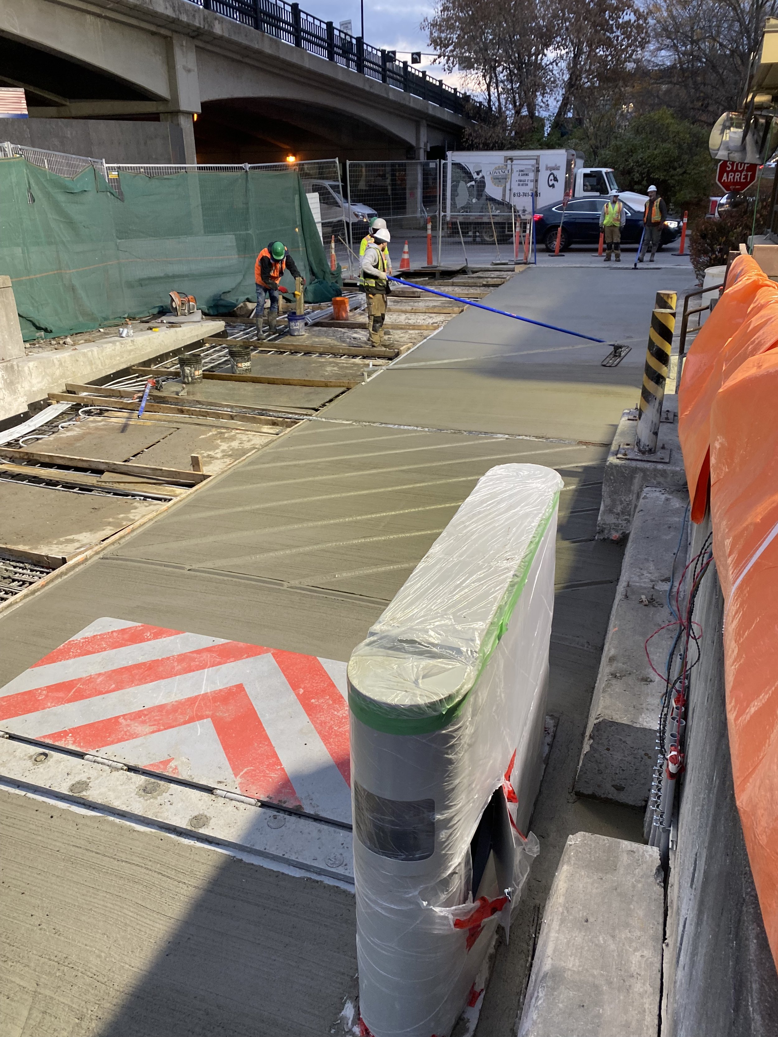 Construction workers smoothing wet concrete on a road under a bridge.