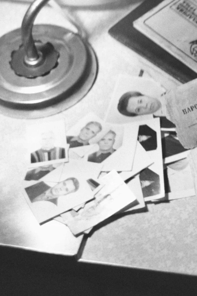 Photographs of several people, a desk lamp, and some documents or magazines on a desk or table.