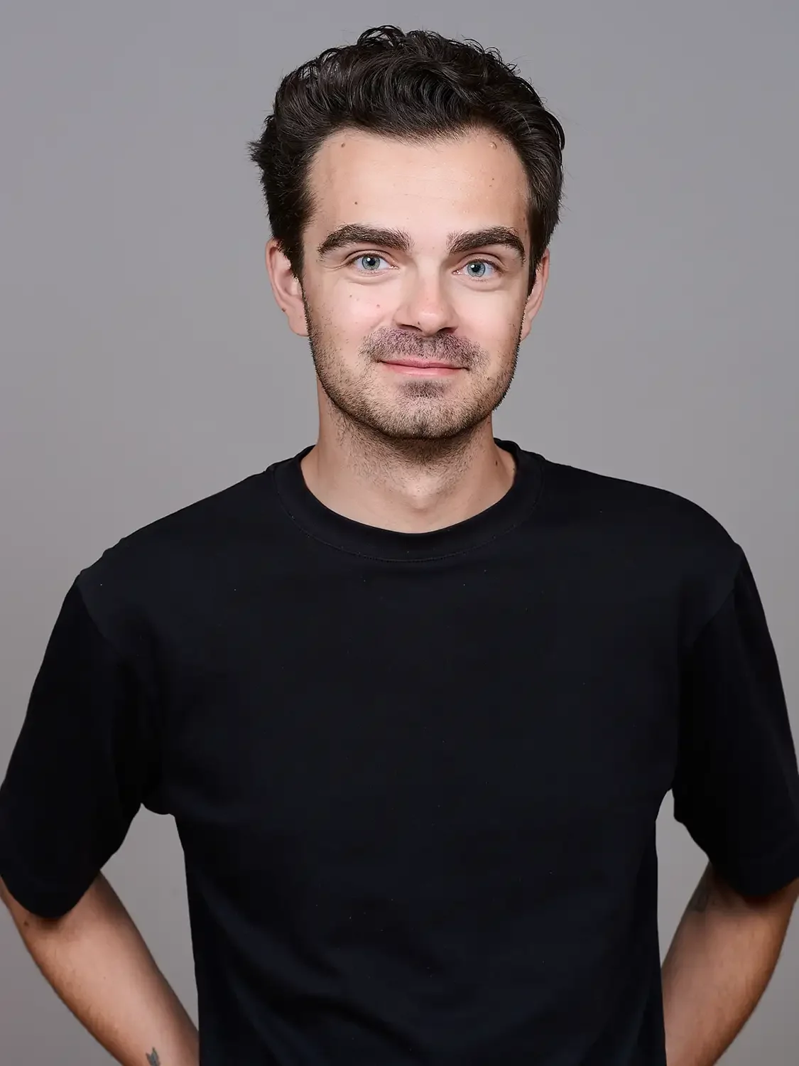 Head-shot of a  young man with brown hair and blue eyes wearing a black t-shirt, photographed in an elegant light photo studio.