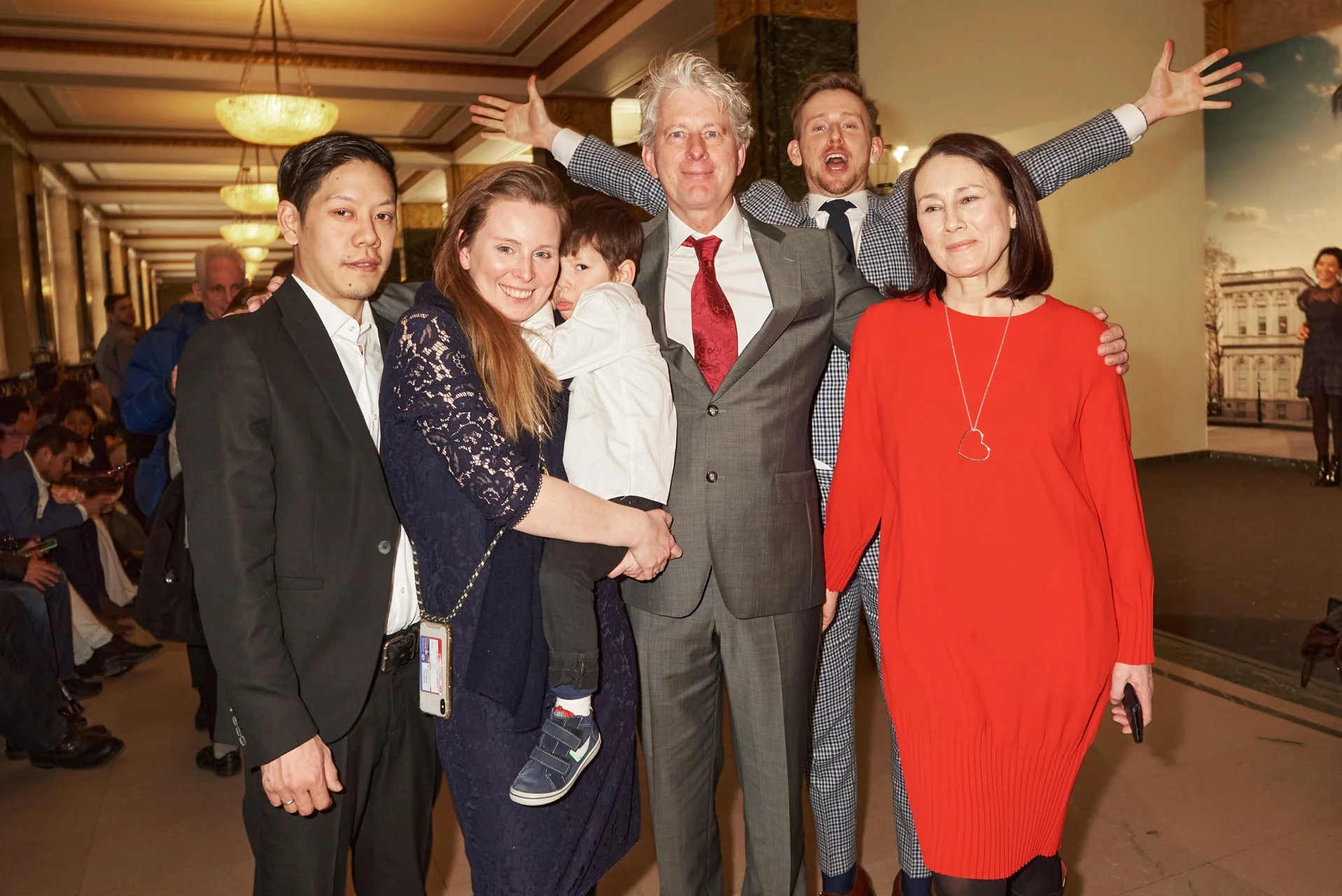 A diverse group of six people, including children and adults, gathered at a formal event in a hotel lobby, posing for a photo together.