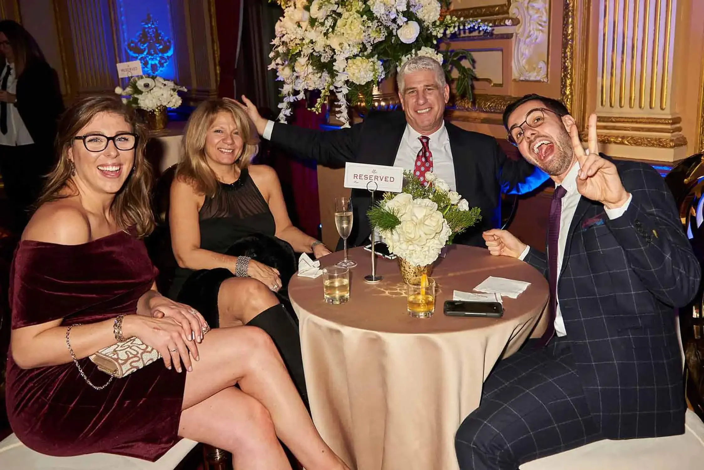 A group of executive  at Workforce corporate party, sitting at a round table with floral centerpieces, smiling and posing for the camera. They are dressed in elegant attire.
