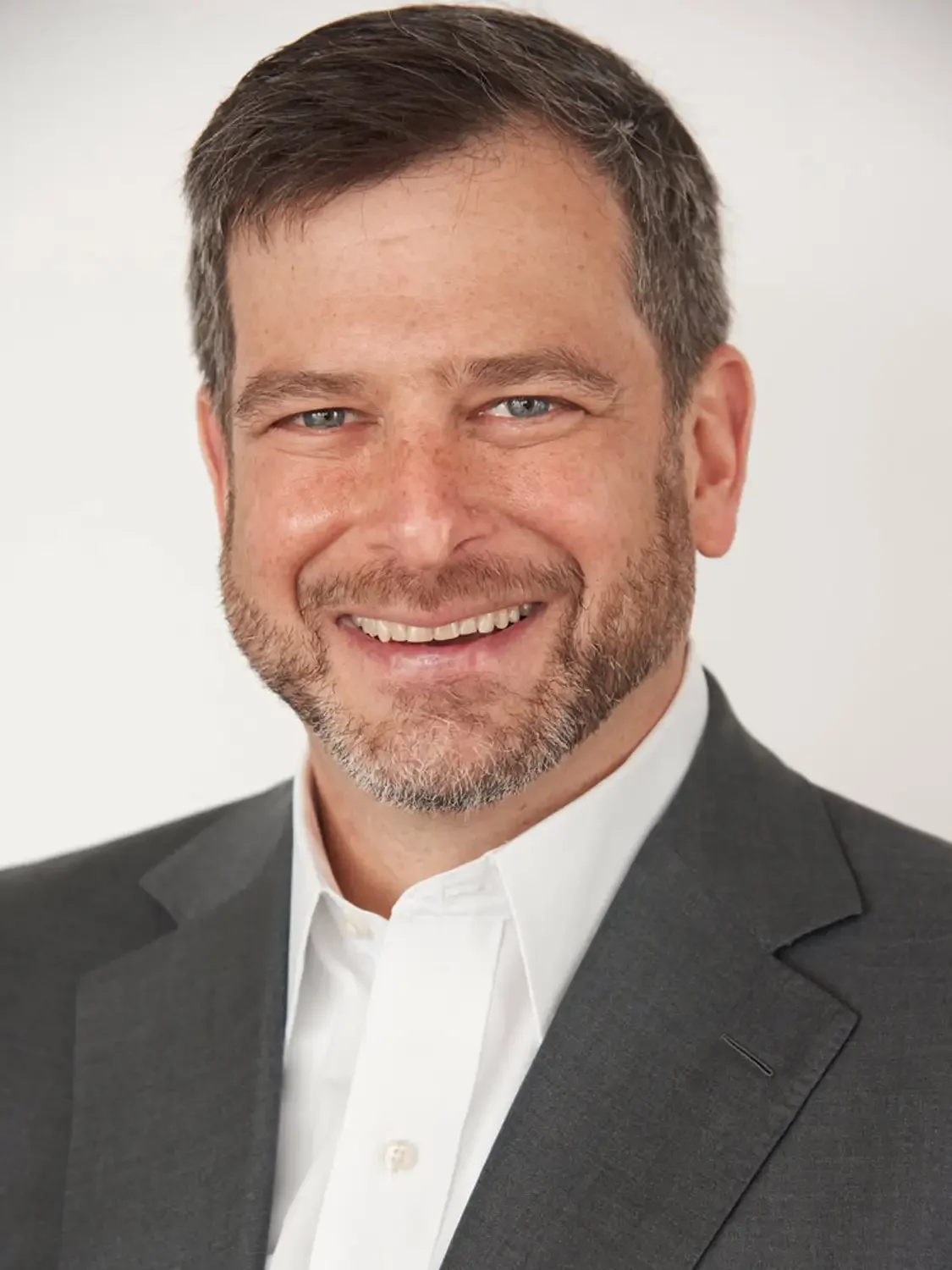 Creative director portrait photographed in natural window light, smiling with short brown hair, blue eyes, and a beard. 