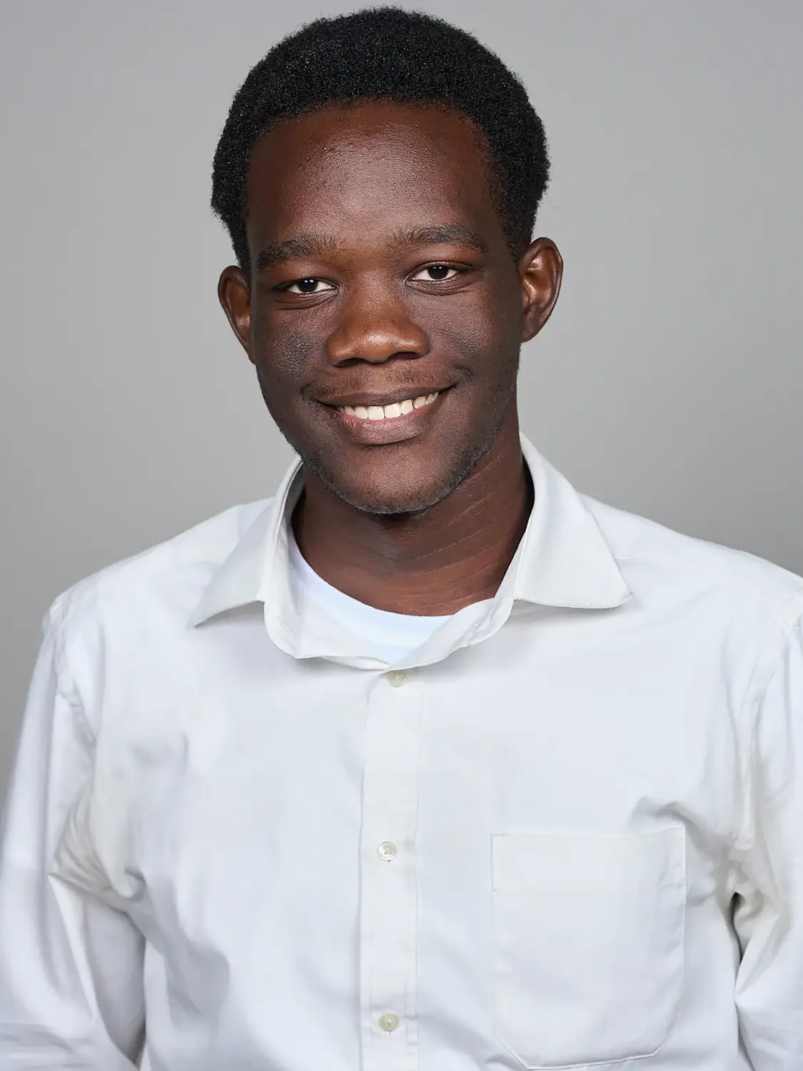 Portrait of a smiling young African American man with short curly hair, wearing a white collared shirt. Photographed in a professional photo studio.