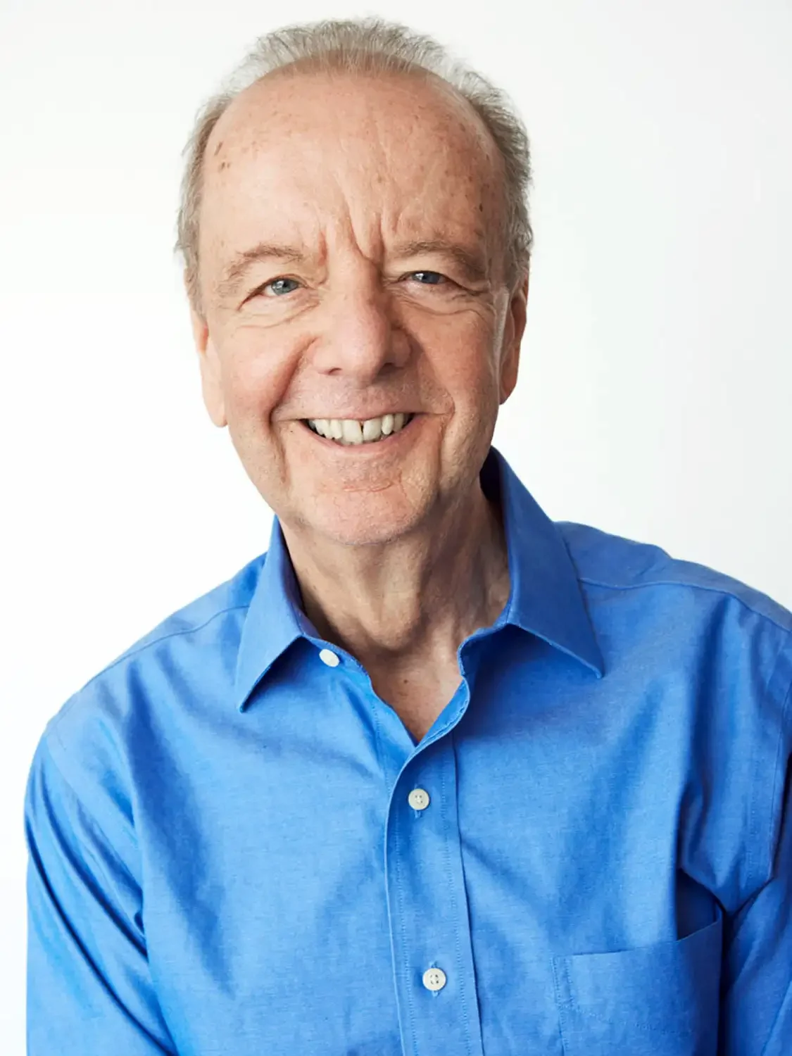 Corporate Headshot of a senior executive with gray hair wearing a bright blue dress shirt against a plain white background.