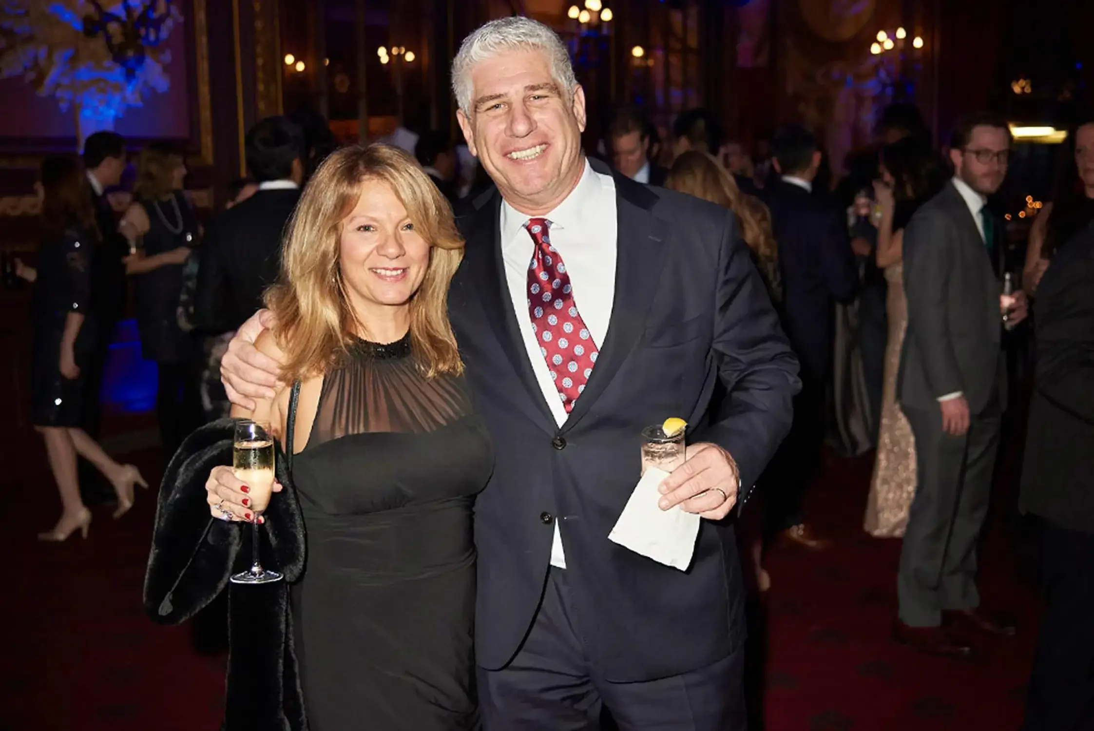 A man and a woman in an elegant fancy venue for a corporate event.They are smiling and holding glasses of champagne.