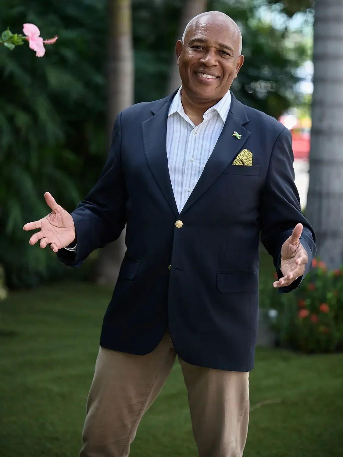 Professional portrait of a senior executive  in a formal attire, standing outdoors with a green garden background, displaying energy and confidence.