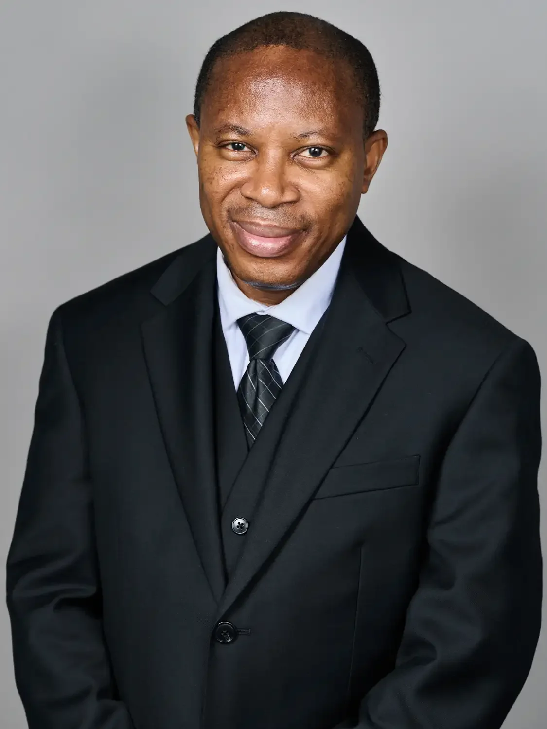 Professional headshot of a senior black man in a black suit, white shirt, and black striped tie, in. beautiful studio lighting.