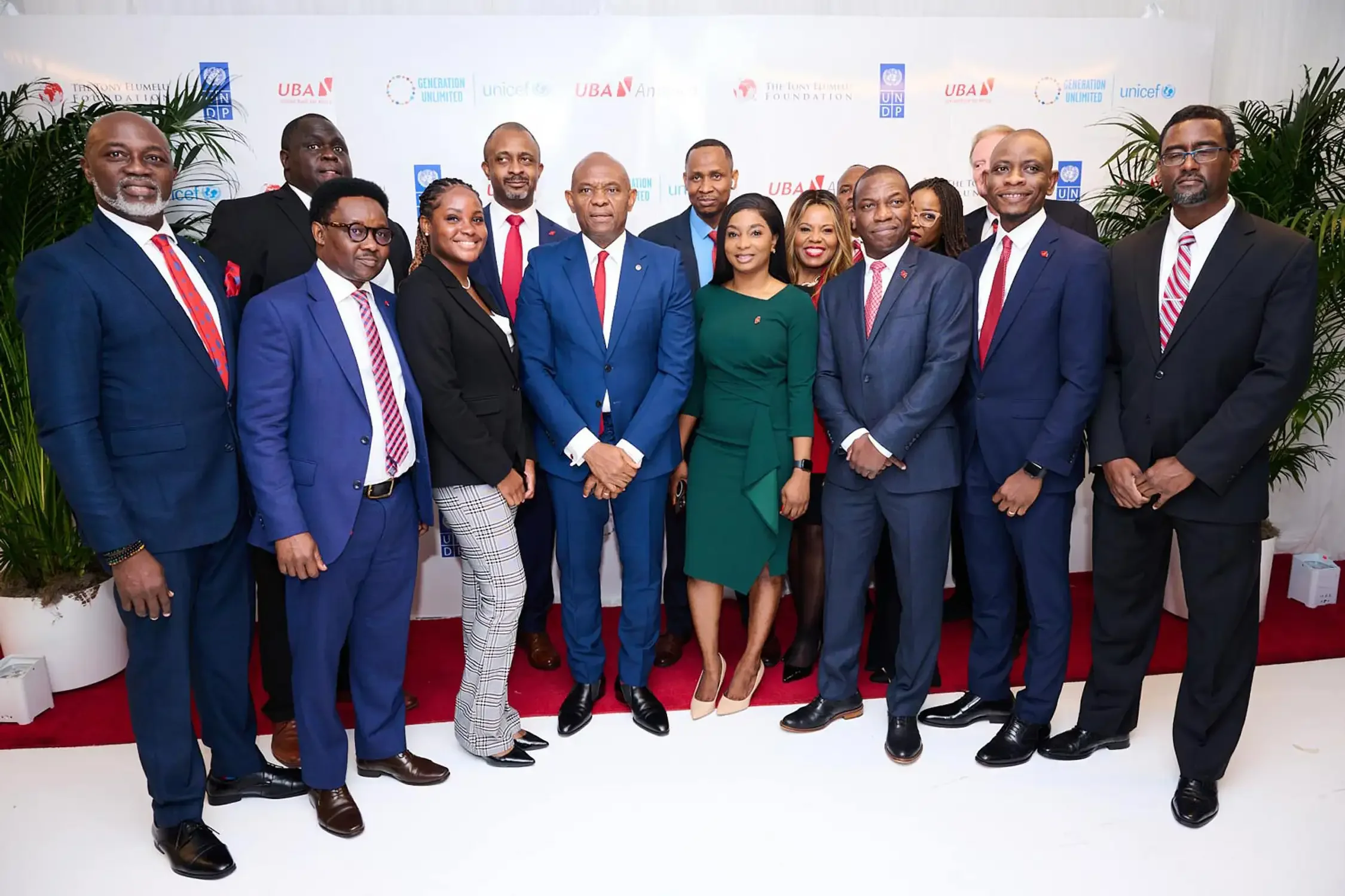 Event photo of a group of professionally dressed men and women smiling at an indoor event, standing on a red carpet with a backdrop featuring logos from UNDP, UNICEF, UBA.