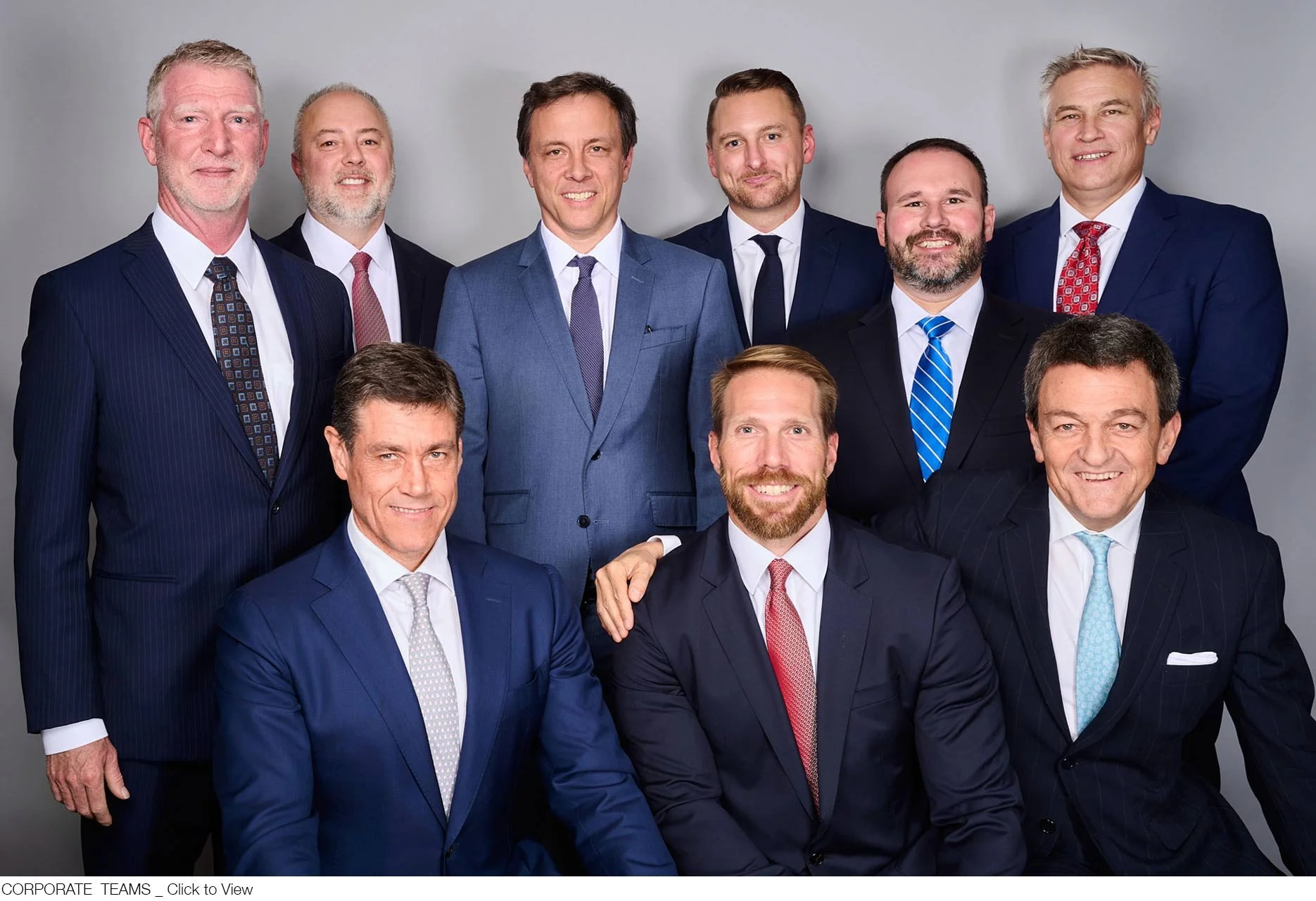 An executive group of ten men in business suits posing for a formal photo against in a studio.