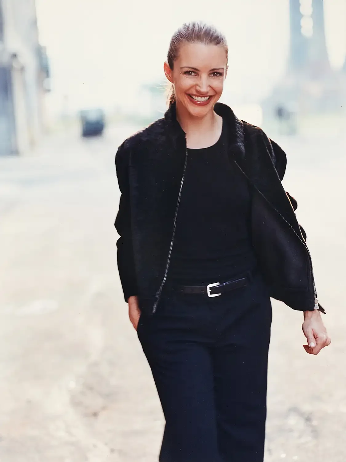 Kirsten Davis walking outdoors in urban setting, wearing black jacket and pants.