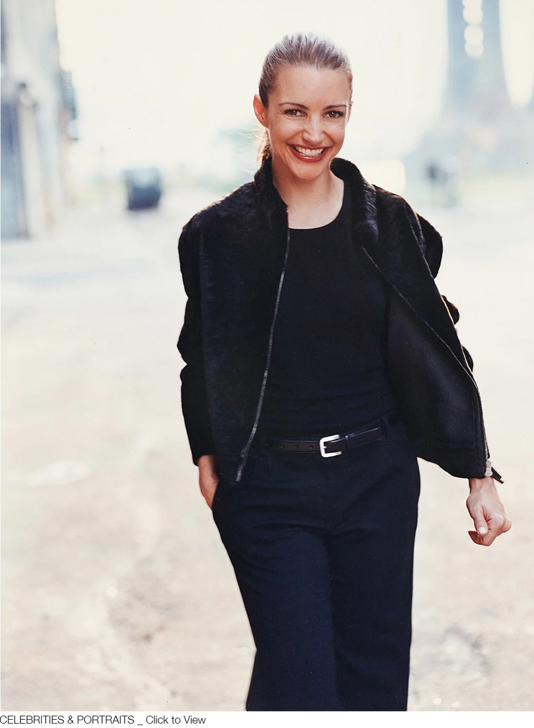 Kristen Davis smiling, dressed in black, standing outdoors on a sunny day.