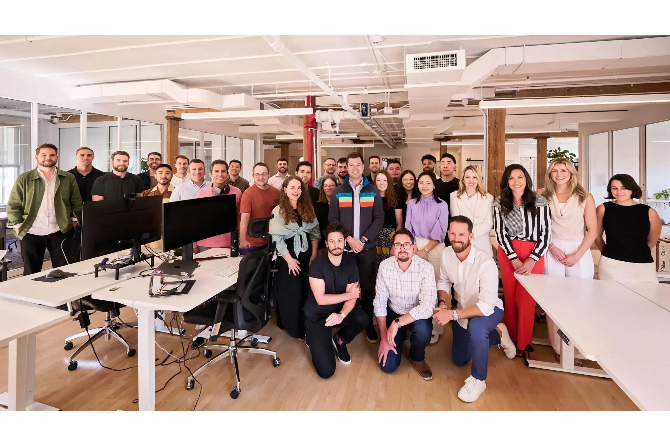 Large group of diverse young adults smiling for a team photo in a modern office space.