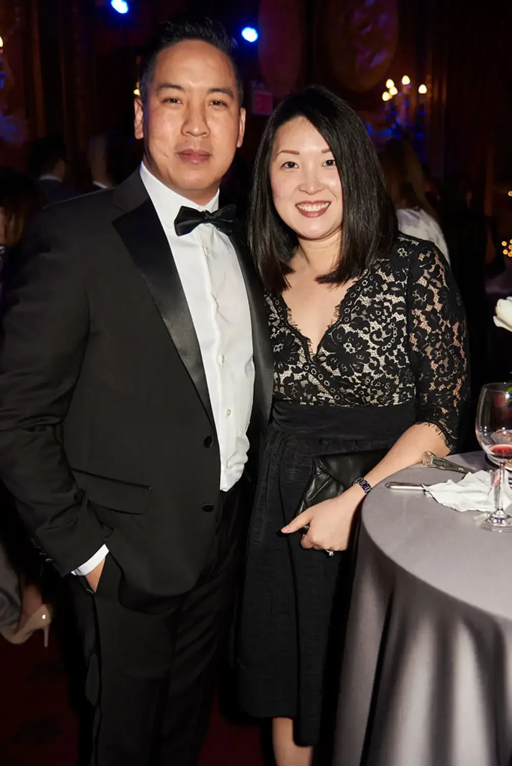A man in a tuxedo and a woman in a black lace dress standing together at a formal corporate event.