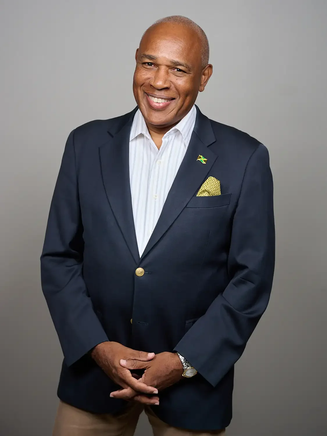 Professional studio headshot of a senior executive  in a dark blue suit with a gold pin and a yellow pocket square, smiling, reflecting confidence and charm.