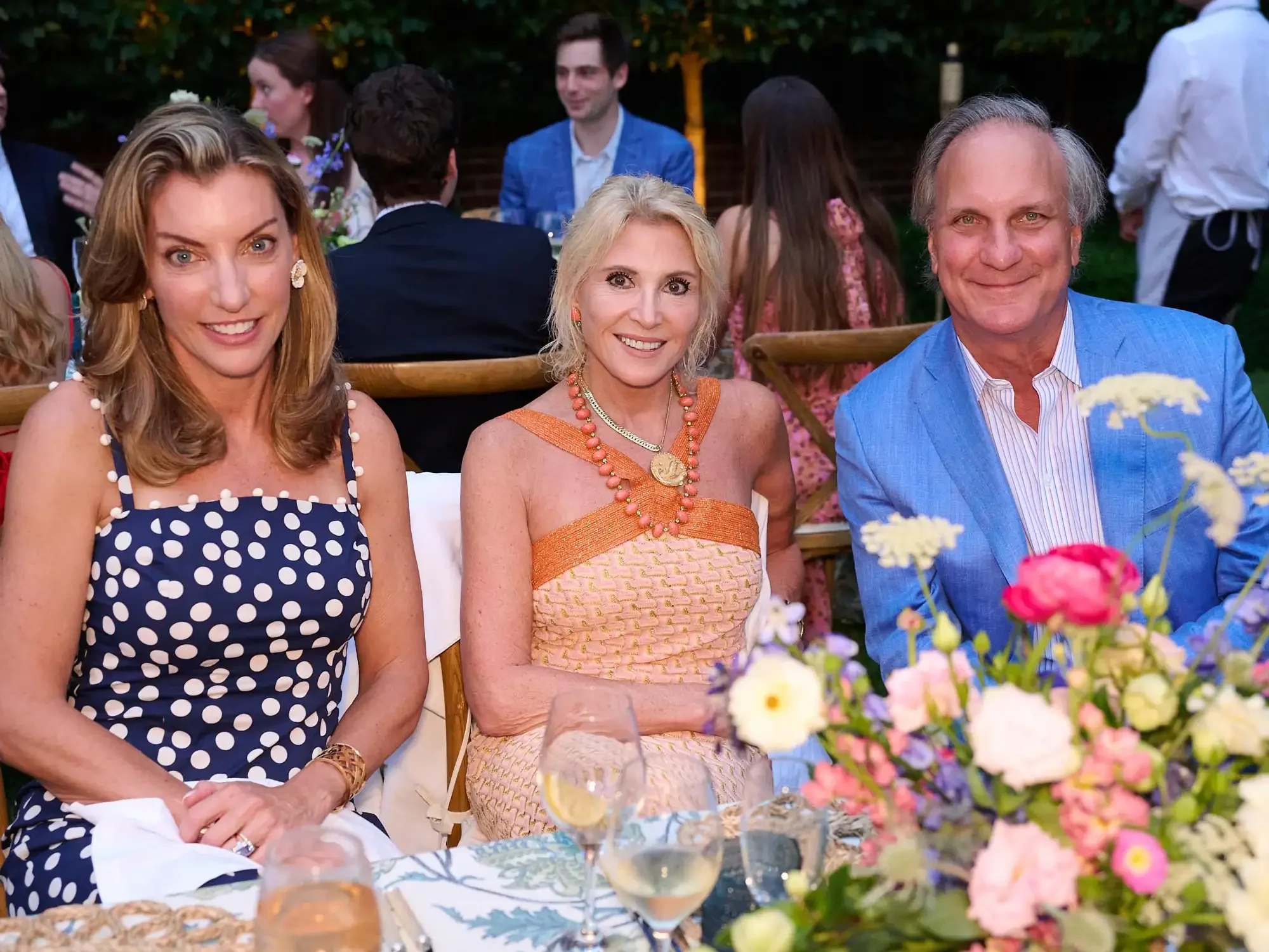 People dining at an outdoor summer party with flowers on the table and in the background.