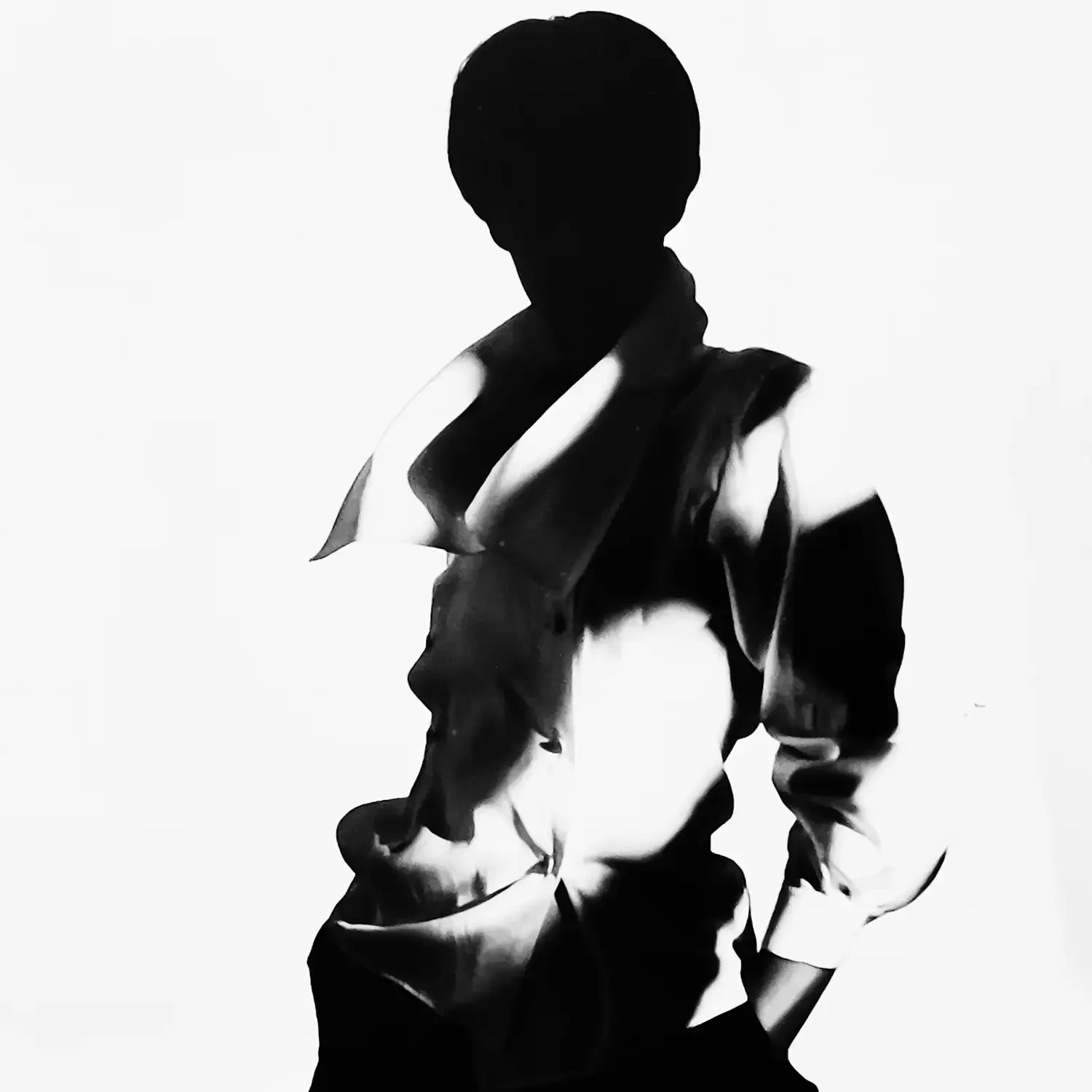Black and white silhouette of a fashion model wearing a white shirt with hands in pockets, photographed in a professional photo studio.