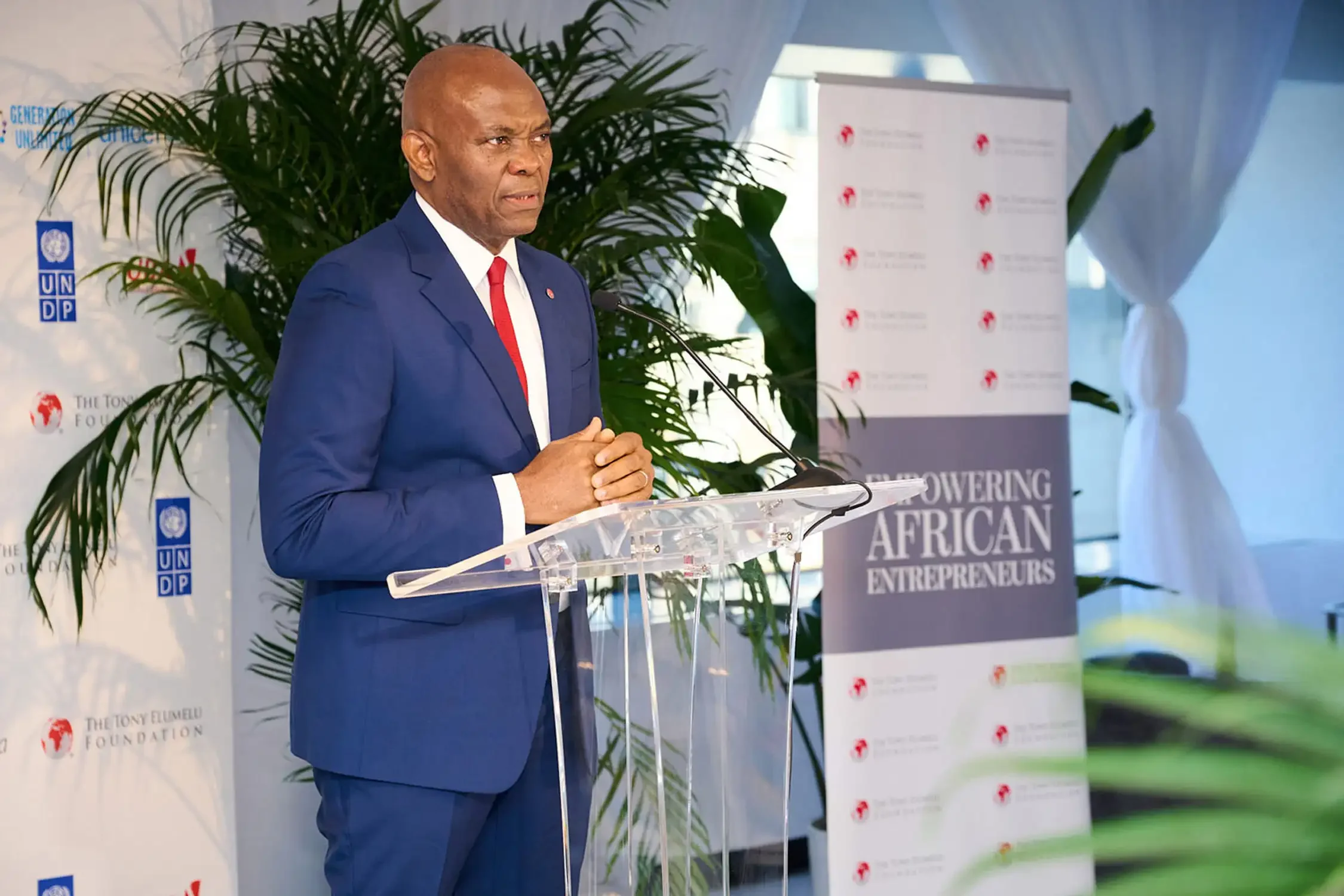 Event photography, a man speaking at a podium with a backdrop. The Tony Elumelu Foundation, and a banner that reads 'Empowering African Entrepreneurs.
