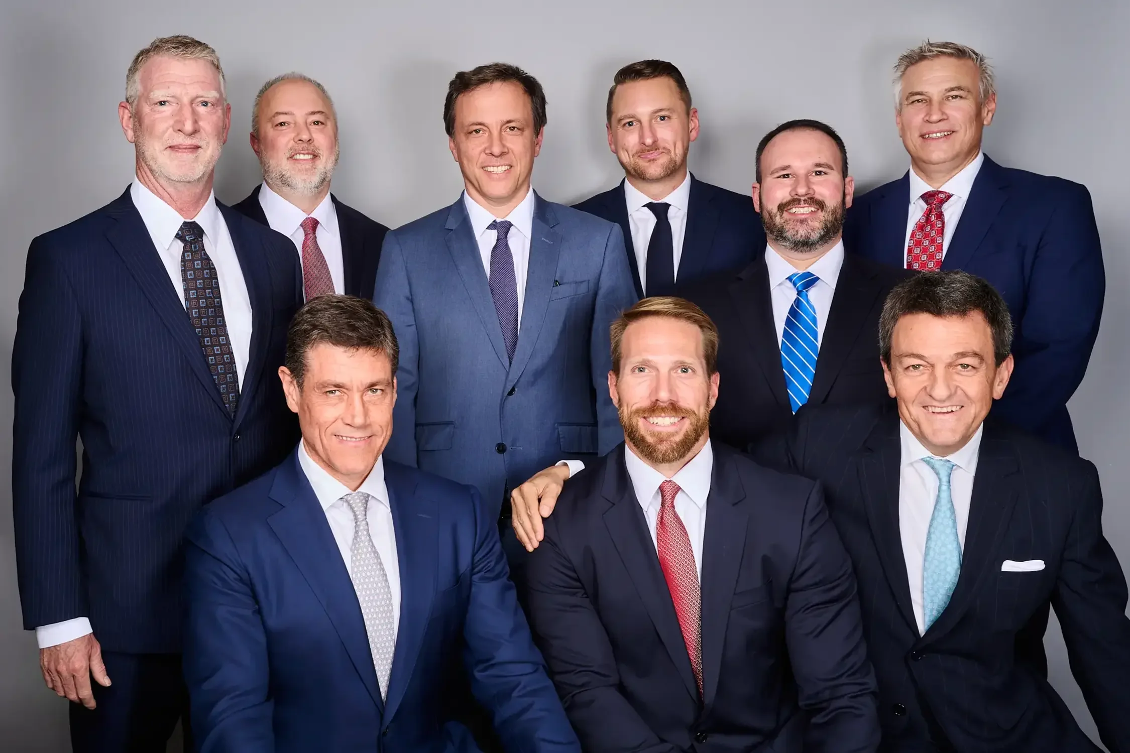 Team portrait of nine executives in formal business attire photographed in a New York photo studio.