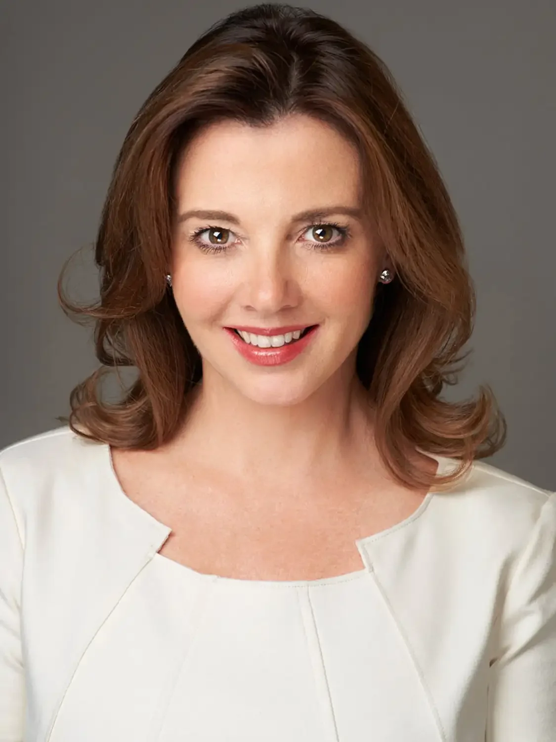Professional headshot of a woman with shoulder-length brown hair, wearing a white dress in photo-studio