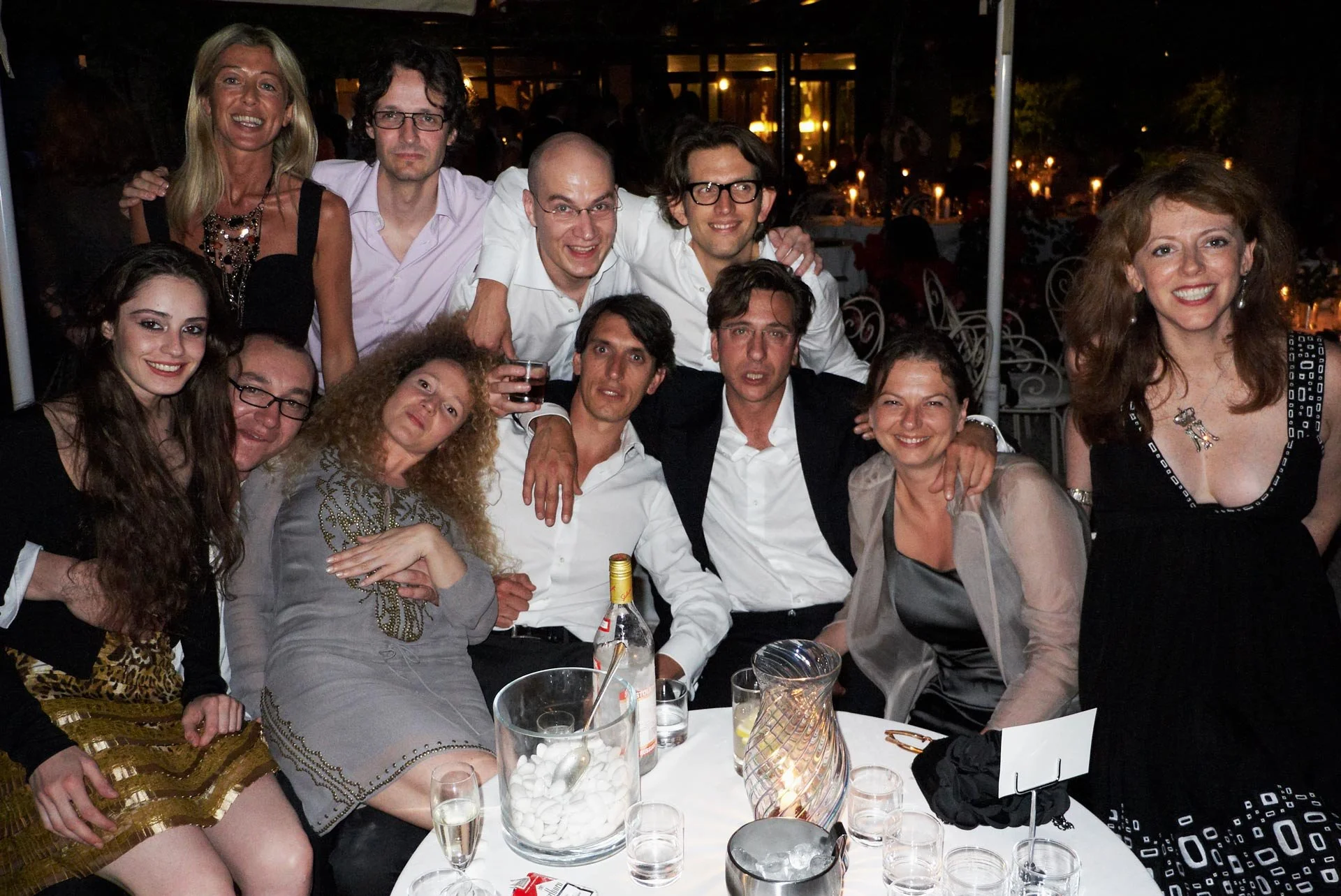 Group of eleven people gathered around a table at a nighttime celebration, smiling and posing for the photo.