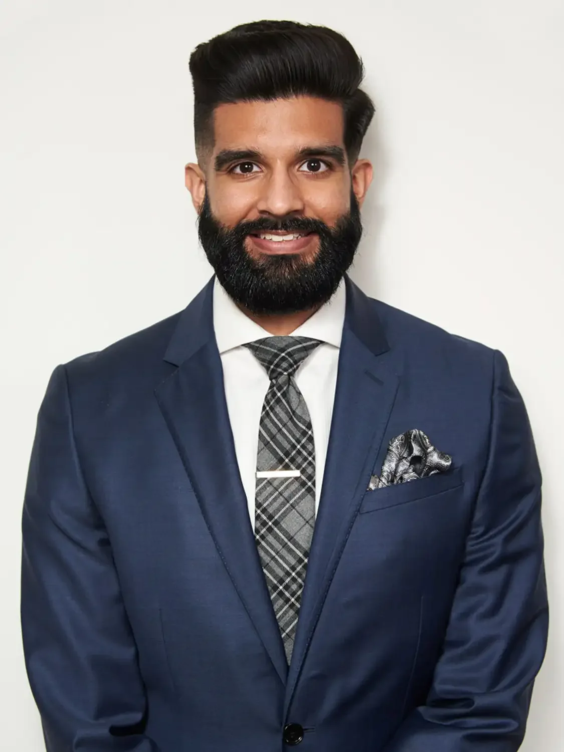 Headshot of a man for eras med school application  with dark hair and a full beard in a navy suit, white shirt, and plaid tie. Photo studio session.