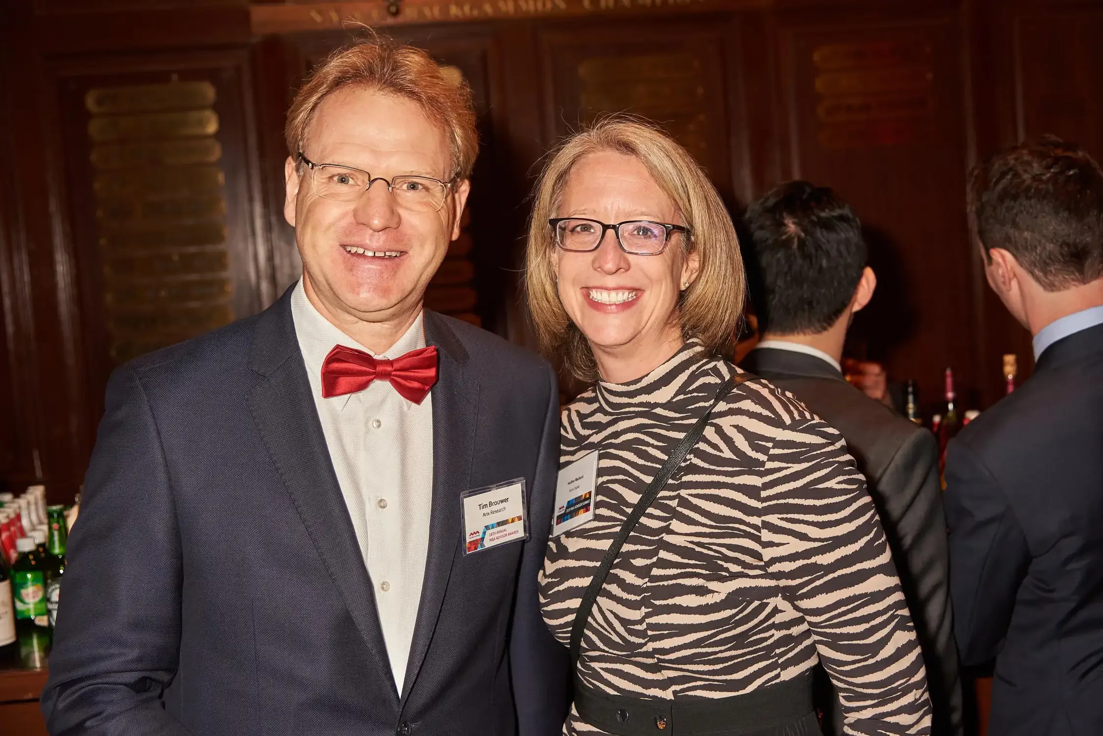 A man and woman attending a corporate event, smiling for the camera. They are in a fancy room with dark wooden walls.