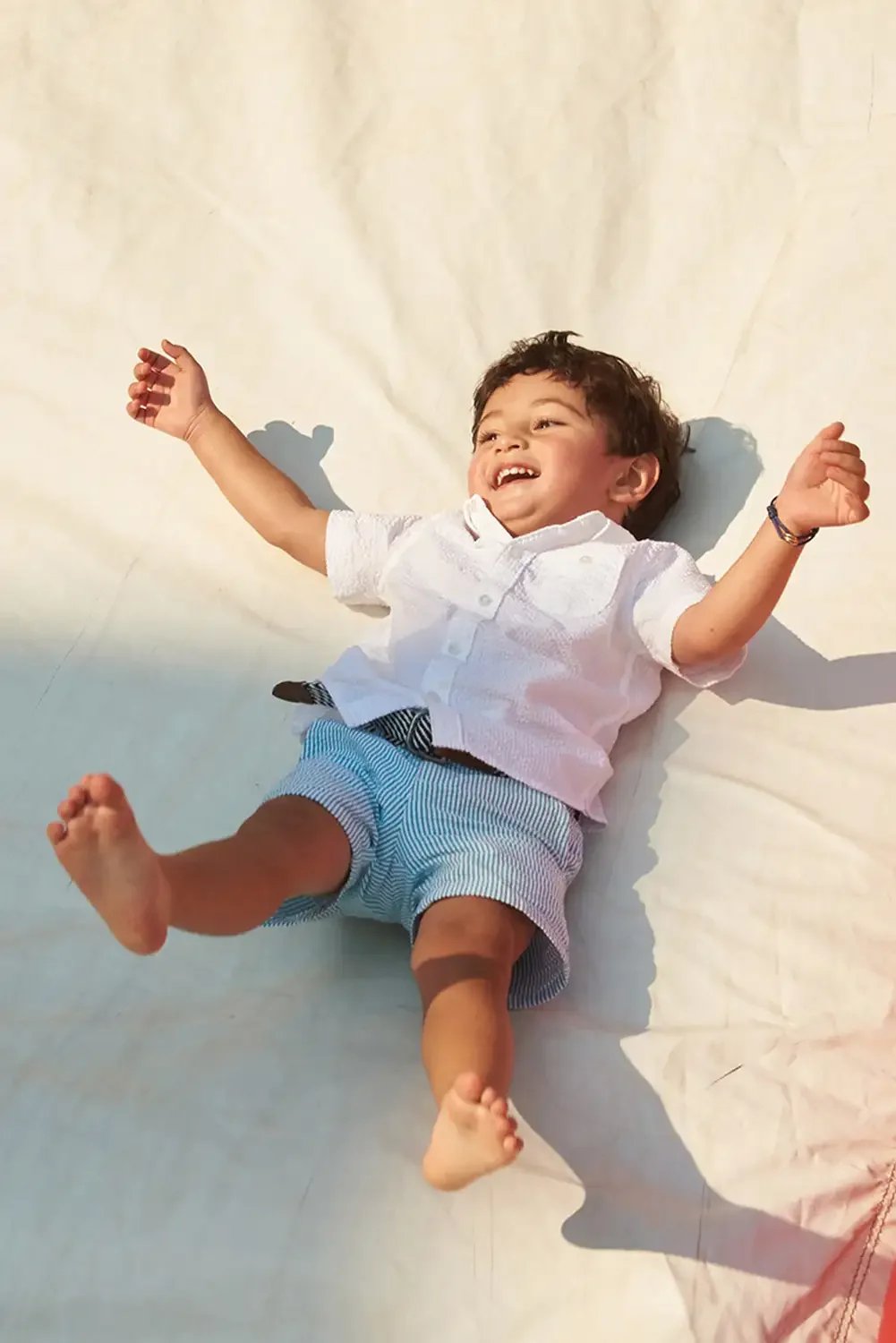 Young boy sliding on a white surface, smiling and playing with his arms and legs spread out.