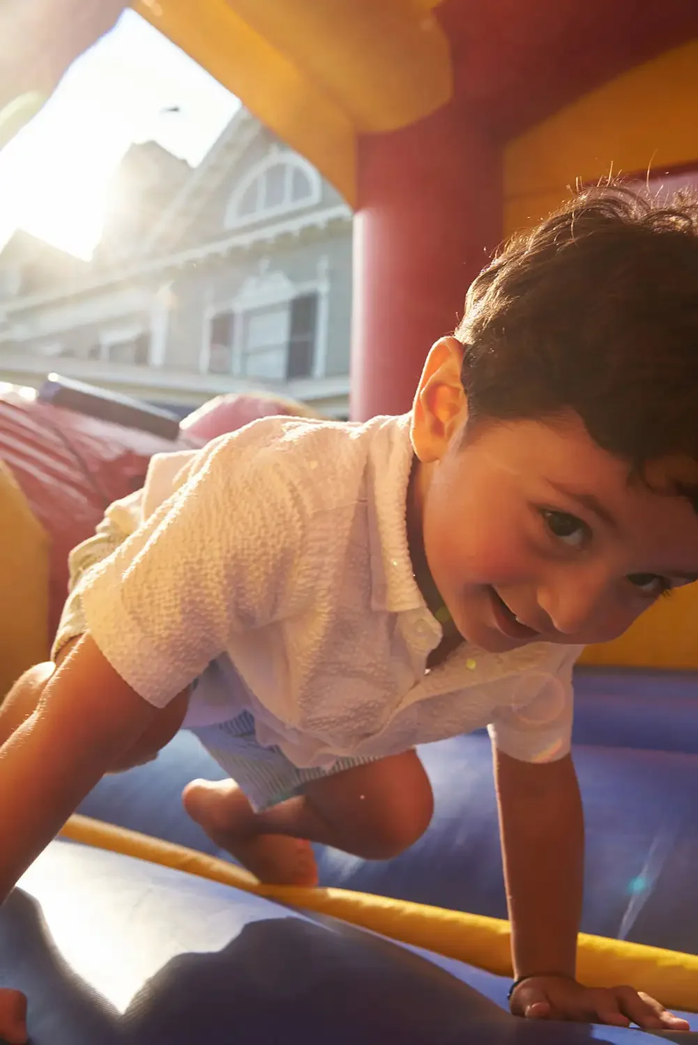 Family photograph of a child crawling on an indoor playground with sunlight streaming through a window in the background.