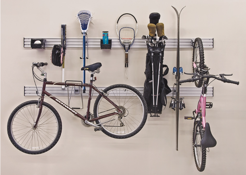 Indoor storage wall with two bicycles, sports rackets, and golf clubs hanging on metal racks.