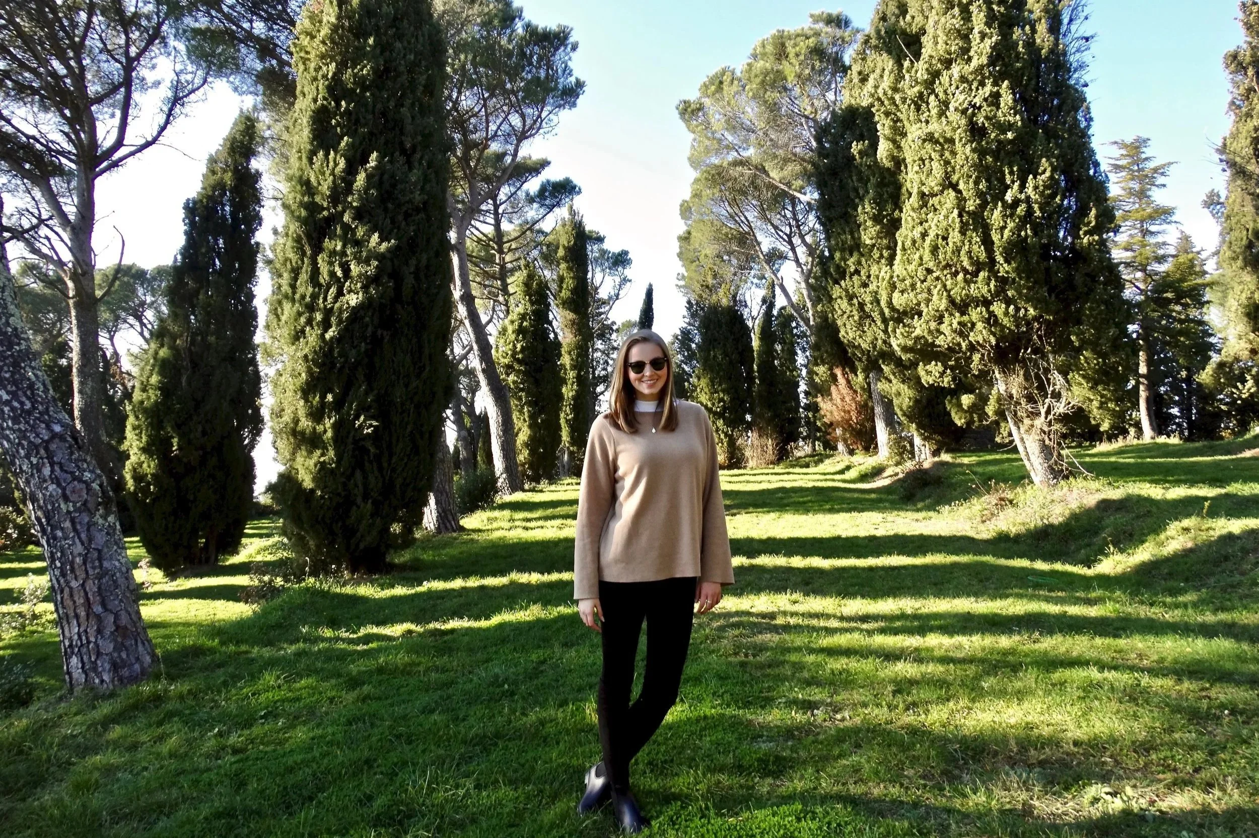 Rachel Robinson walking among cypress trees in the Tuscan countryside, featured in the Supper Atlas Tuscany Two-Week Itinerary