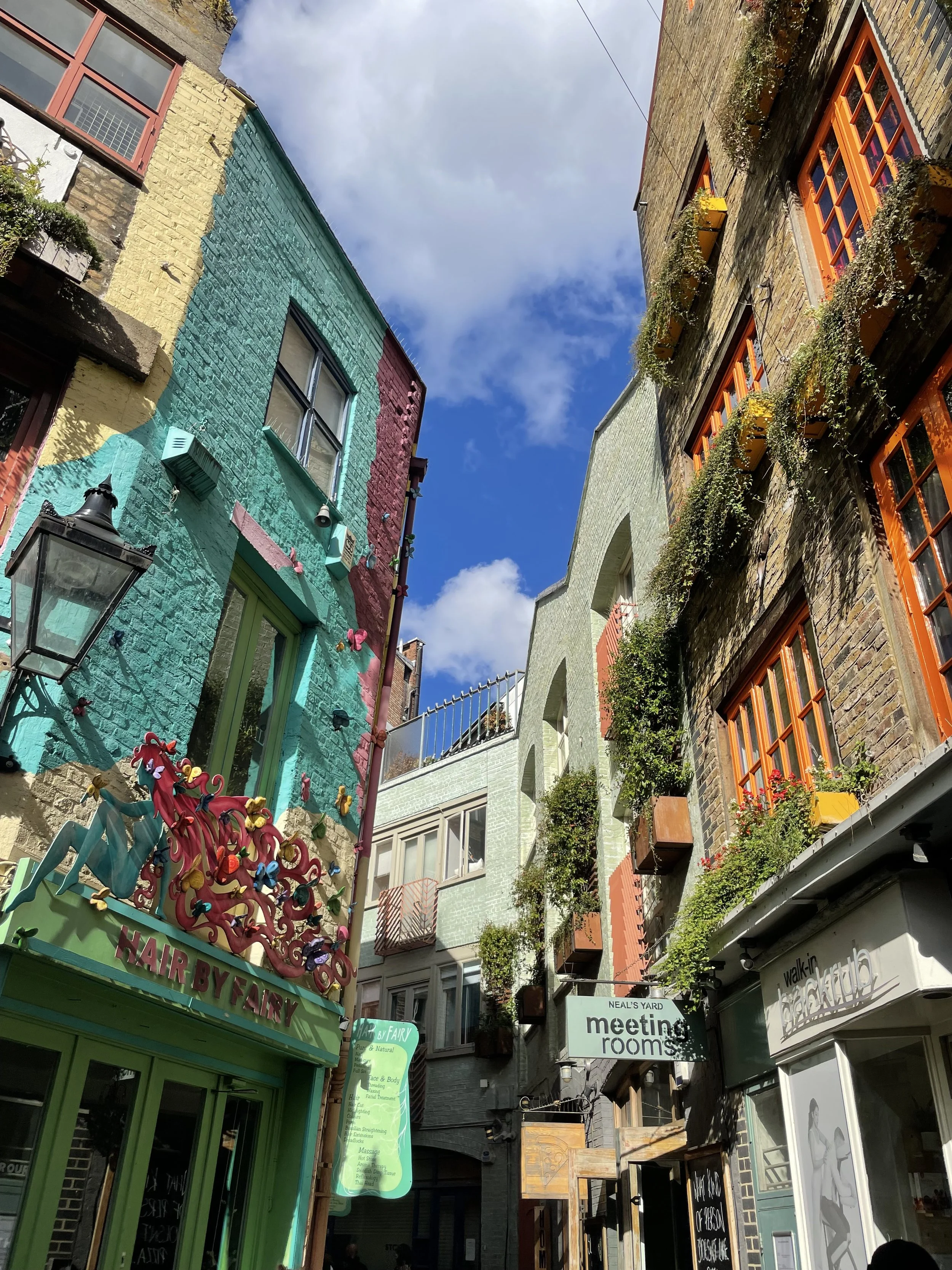 Colorful flower-adorned shopfronts on a cobblestone street in the British Isles, a Supper Atlas travel destination