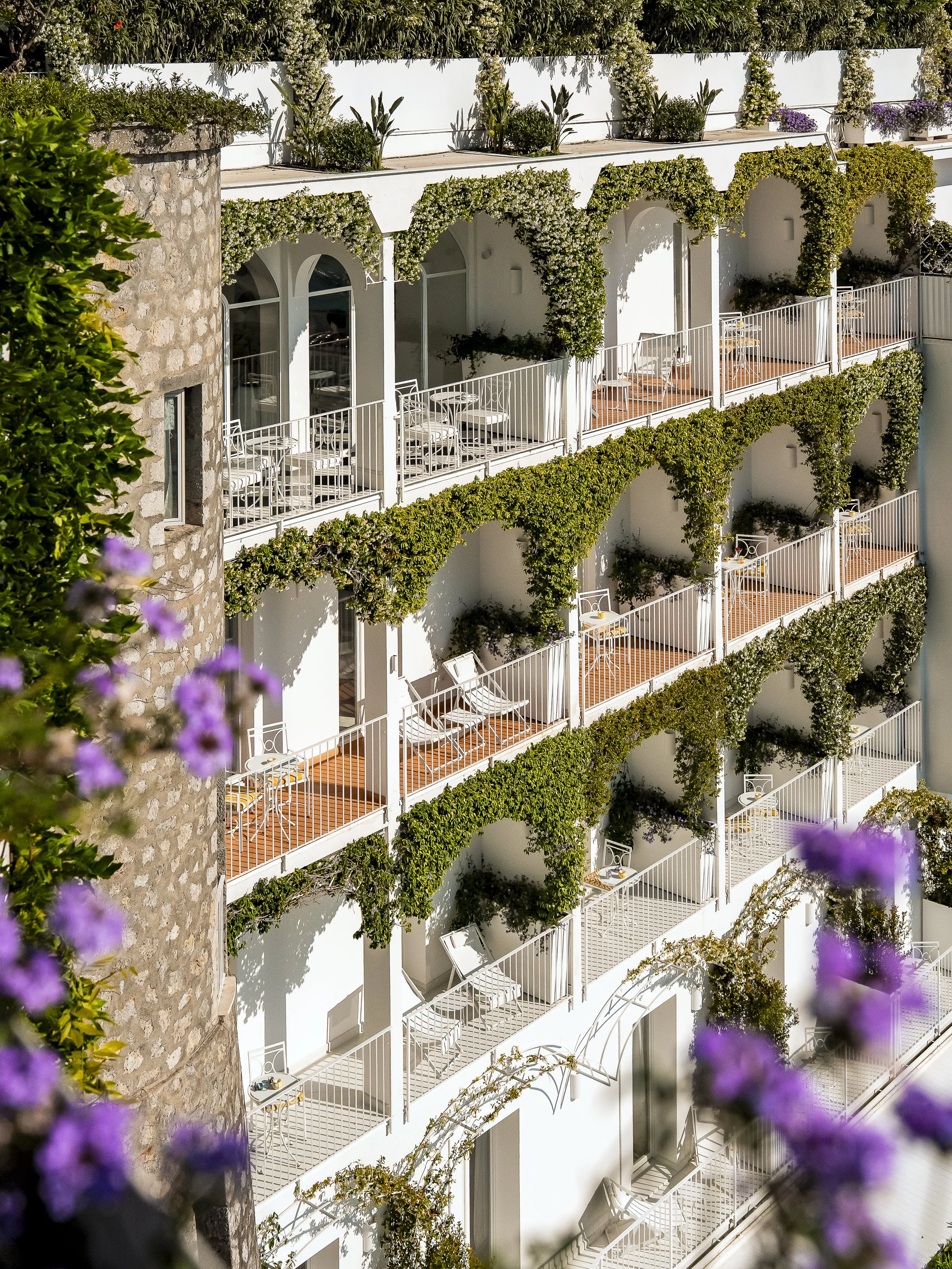 Modern architectural building with tiered white balconies and lush purple flowering plants, evoking the design-forward destinations curated by Supper Atlas
