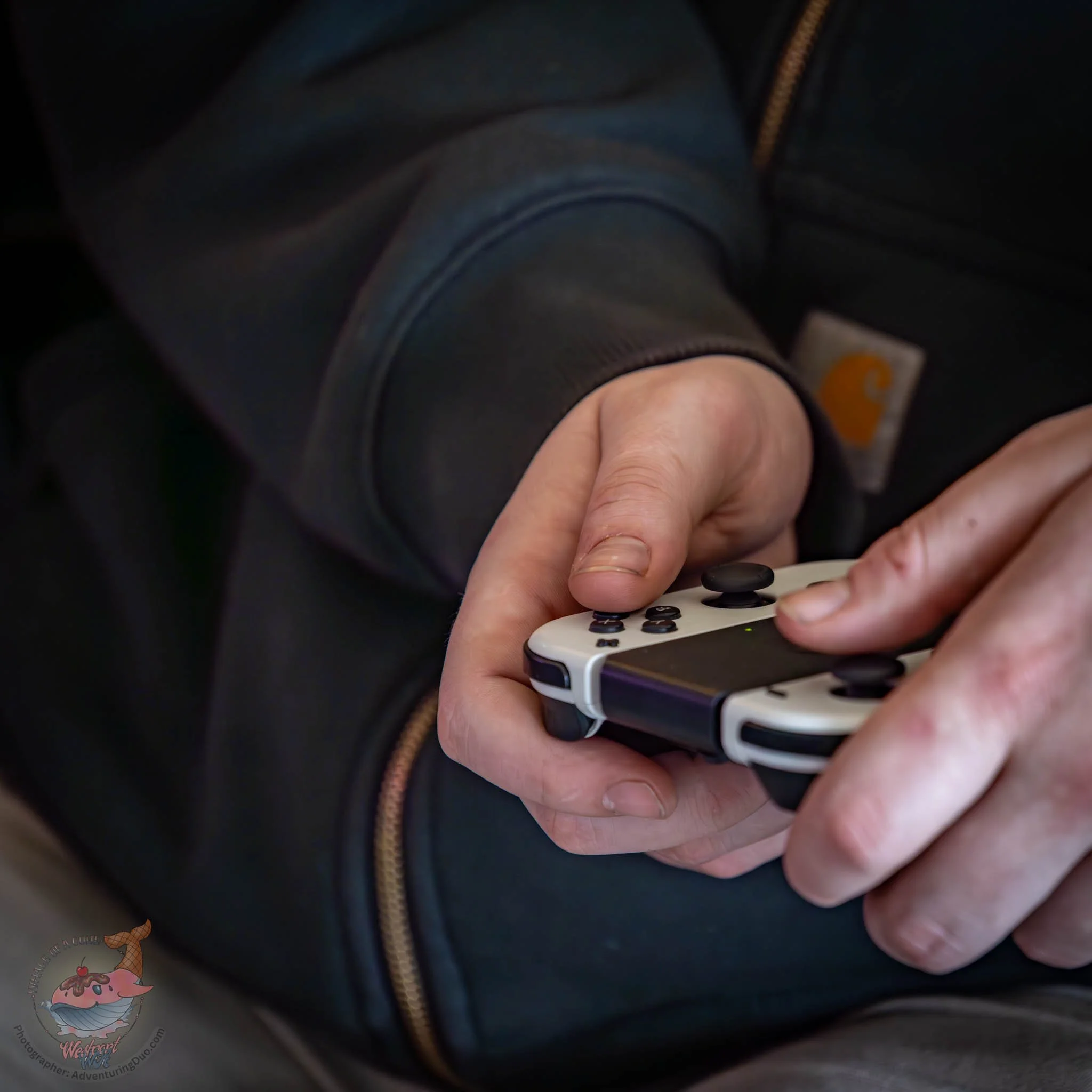 Close-up of a person's hands holding a remote control, with a dark background and part of a jacket visible.