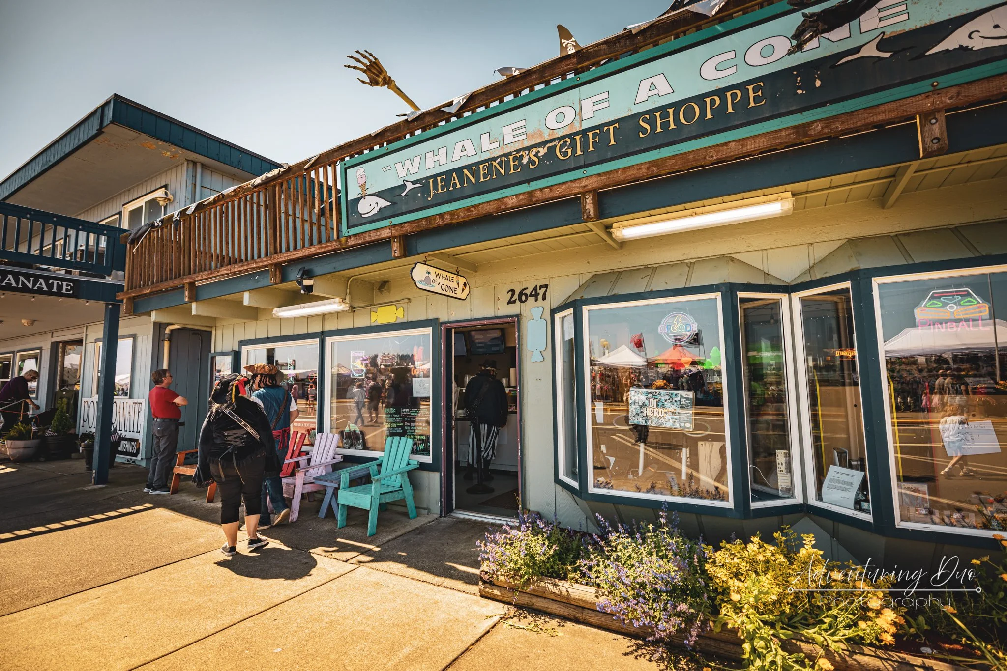Exterior of a gift shop named "Whale of a Cone" with a large sign, showing people walking outside, a flower planter, and neon signs in the windows.