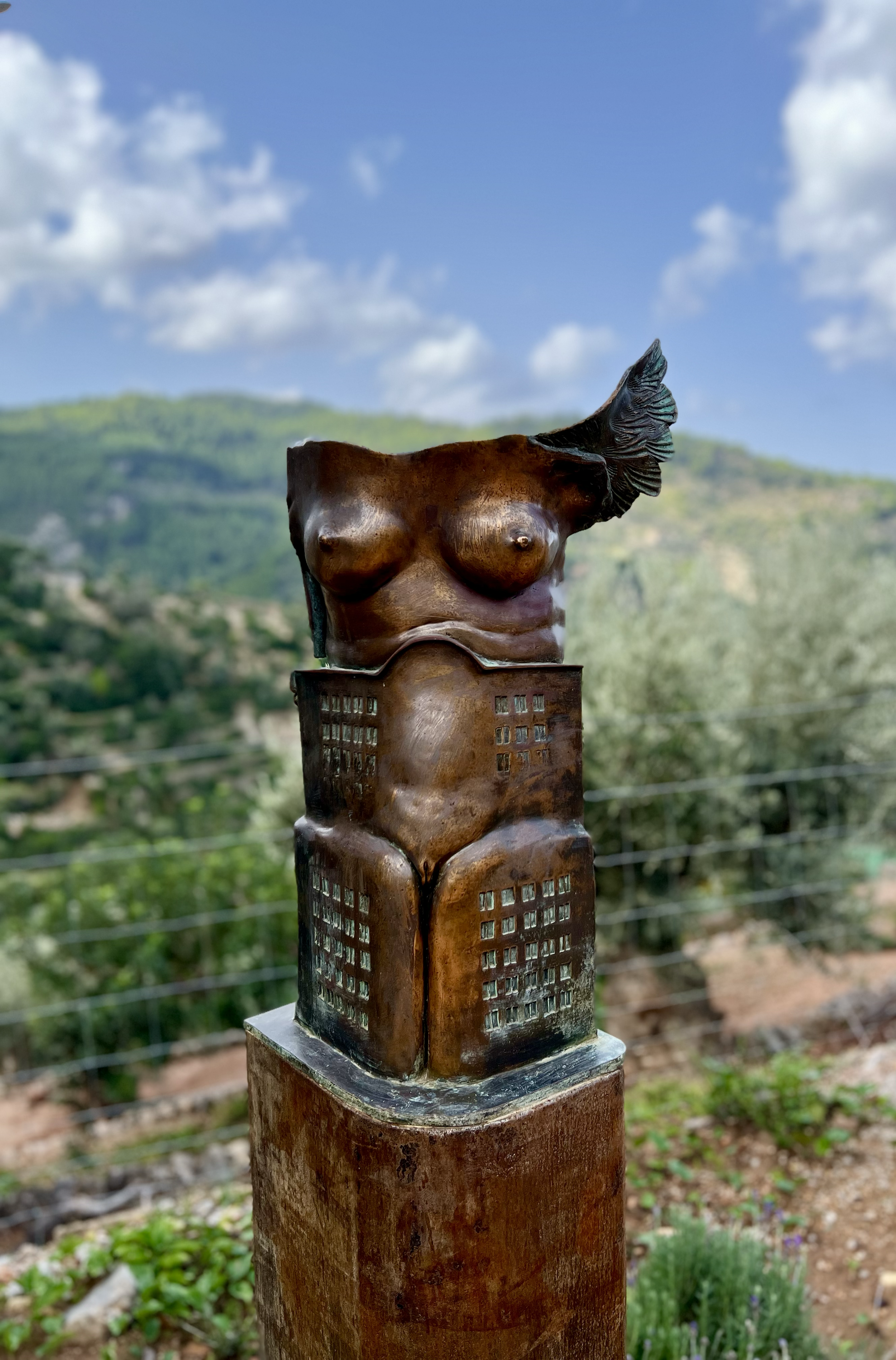 A sculpture of a torso combined with a building structure, situated outdoors with a mountain and trees in the background.