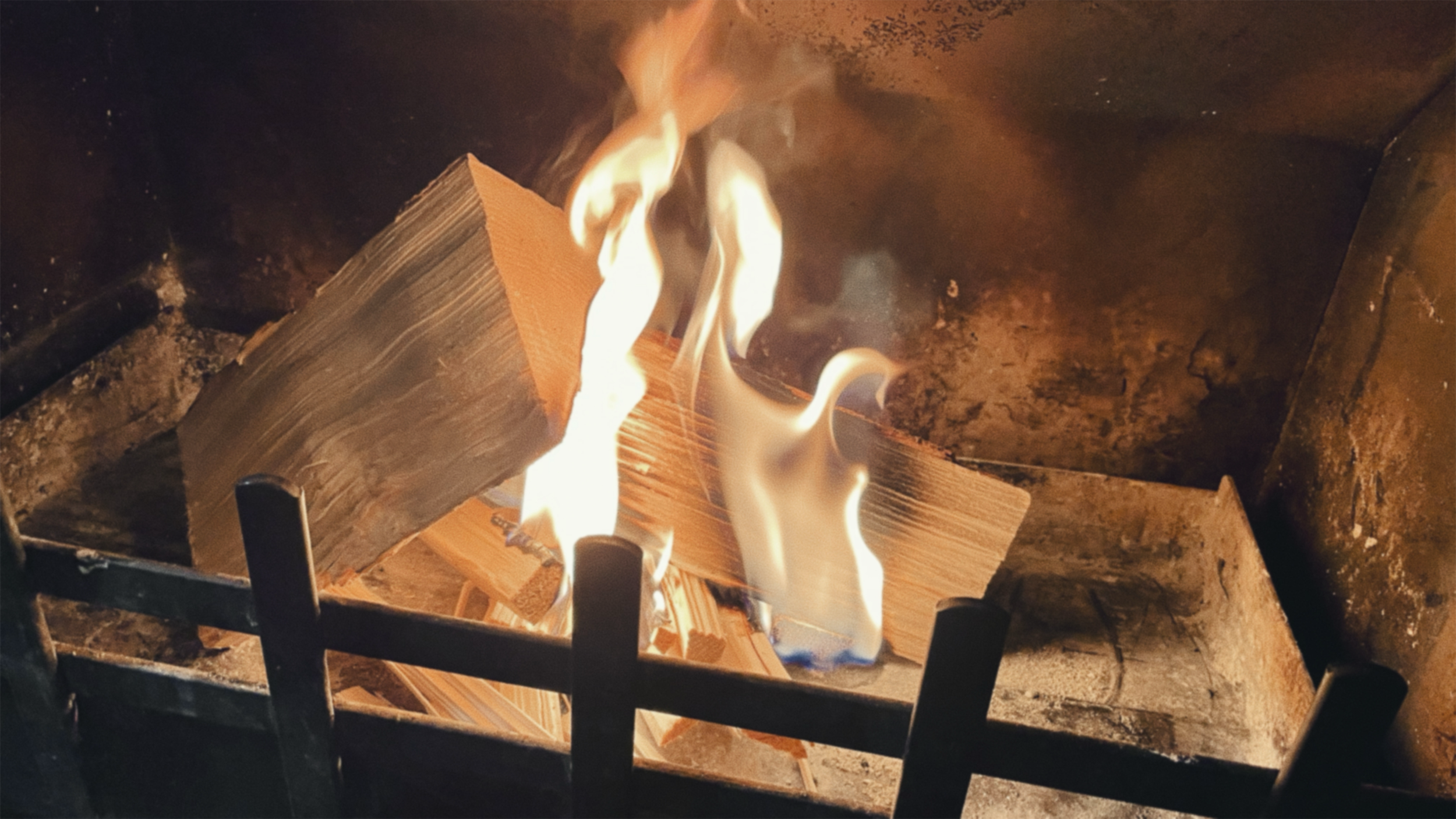 Wood burning on a fireplace grate with orange and yellow flames.