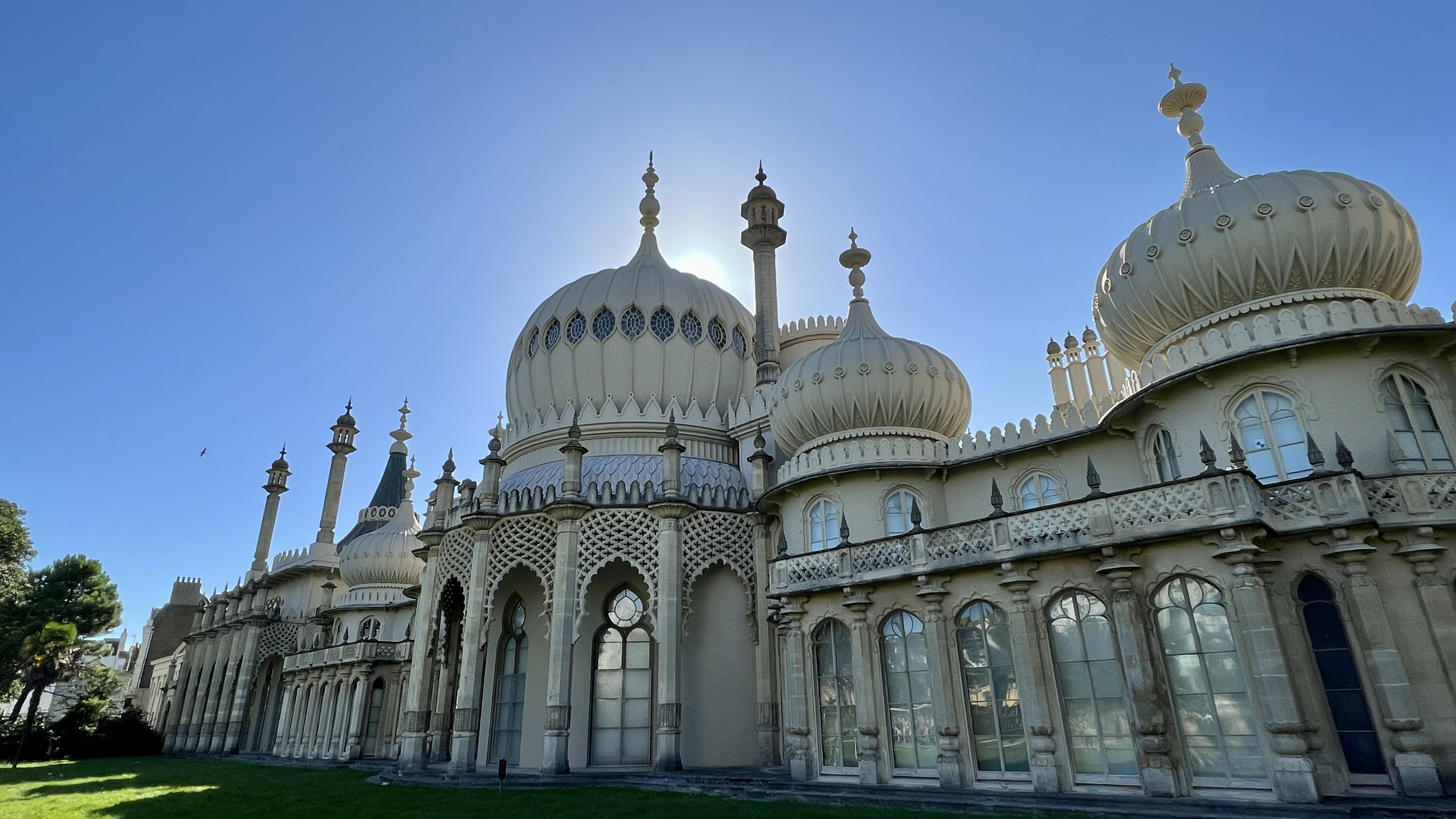The White House, an ornate palace with domes and minarets, is set against a clear blue sky with the sun behind its central dome, creating a halo effect.