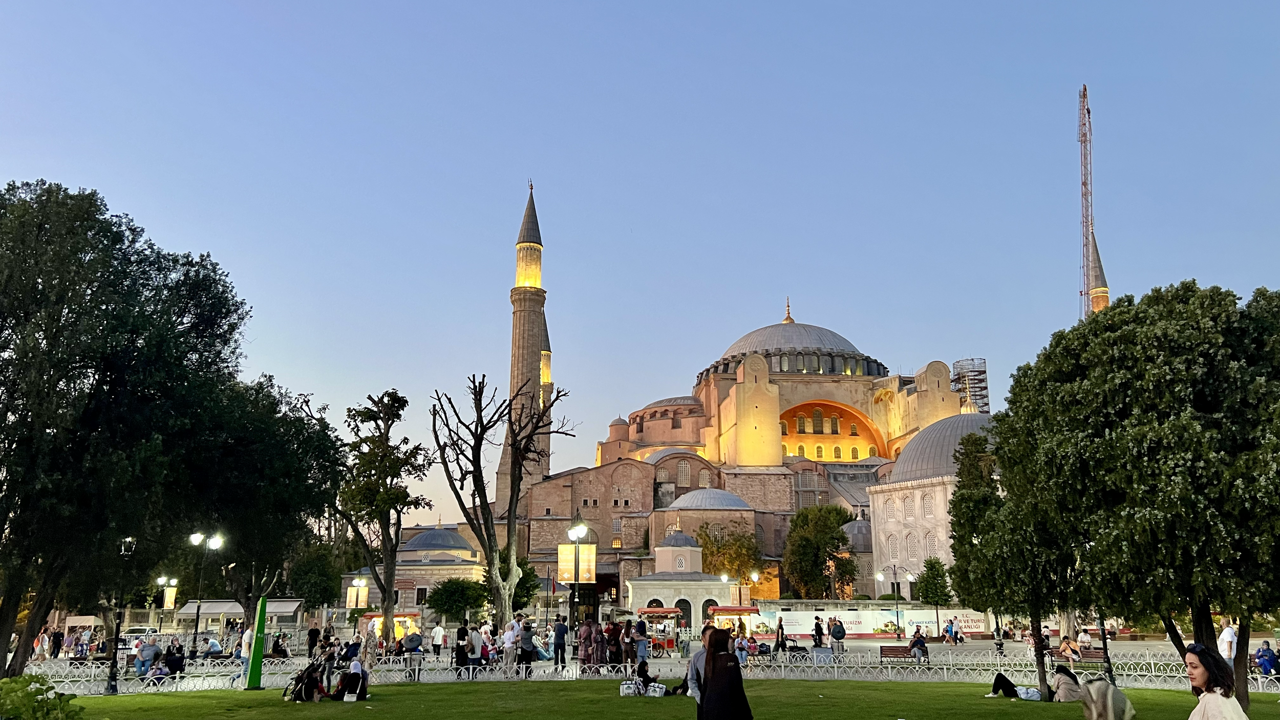 View of Hagia Sophia in Istanbul, Turkey, illuminated at dusk with people in the park in foreground.