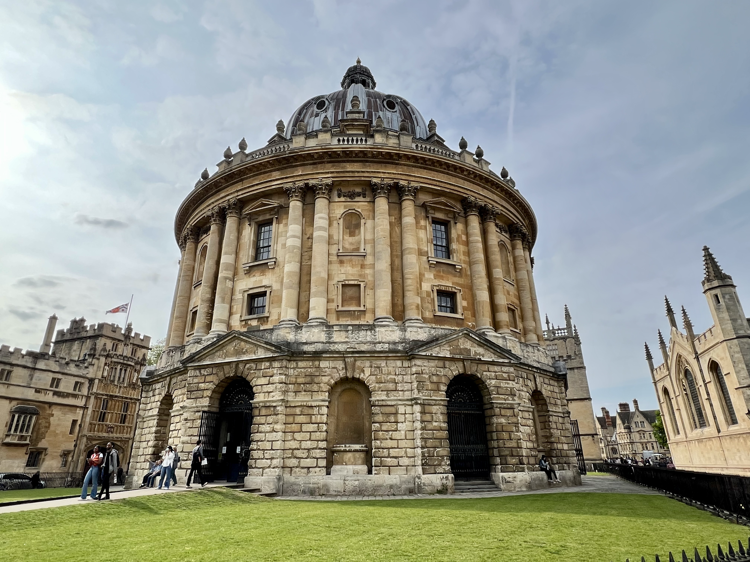 A historic round building with a domed roof, surrounded by a lawn and other old buildings in the background.