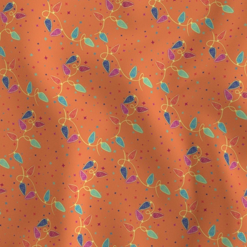 Fabric has bright orange background with twinkling stars in various colors amongst background, string of vintage lightbulbs with lattice design in bright colors of blue,  light blue, green purple, red