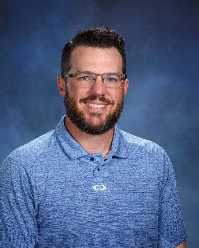 Man in blue polo shirt with brown hair and facial hair, wearing glasses.