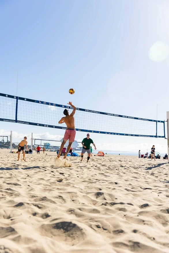 People playing beach volleyball on sandy beach with blue sky