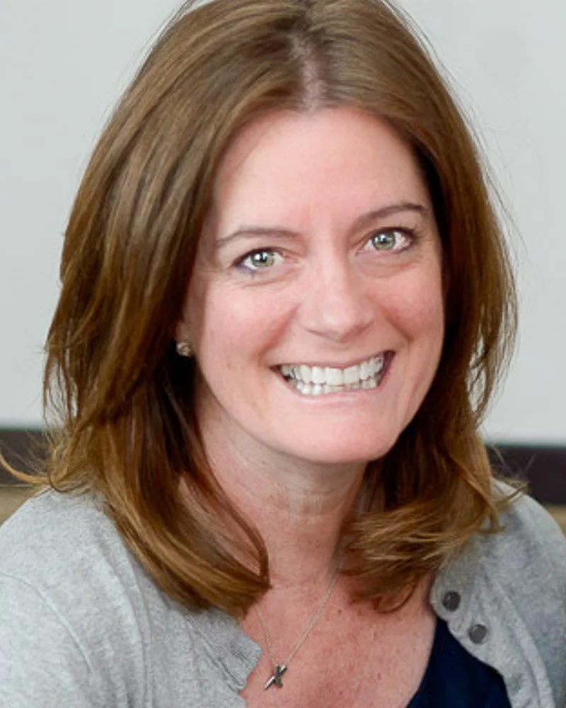Smiling woman with blonde hair wearing a blue shirt outdoors.