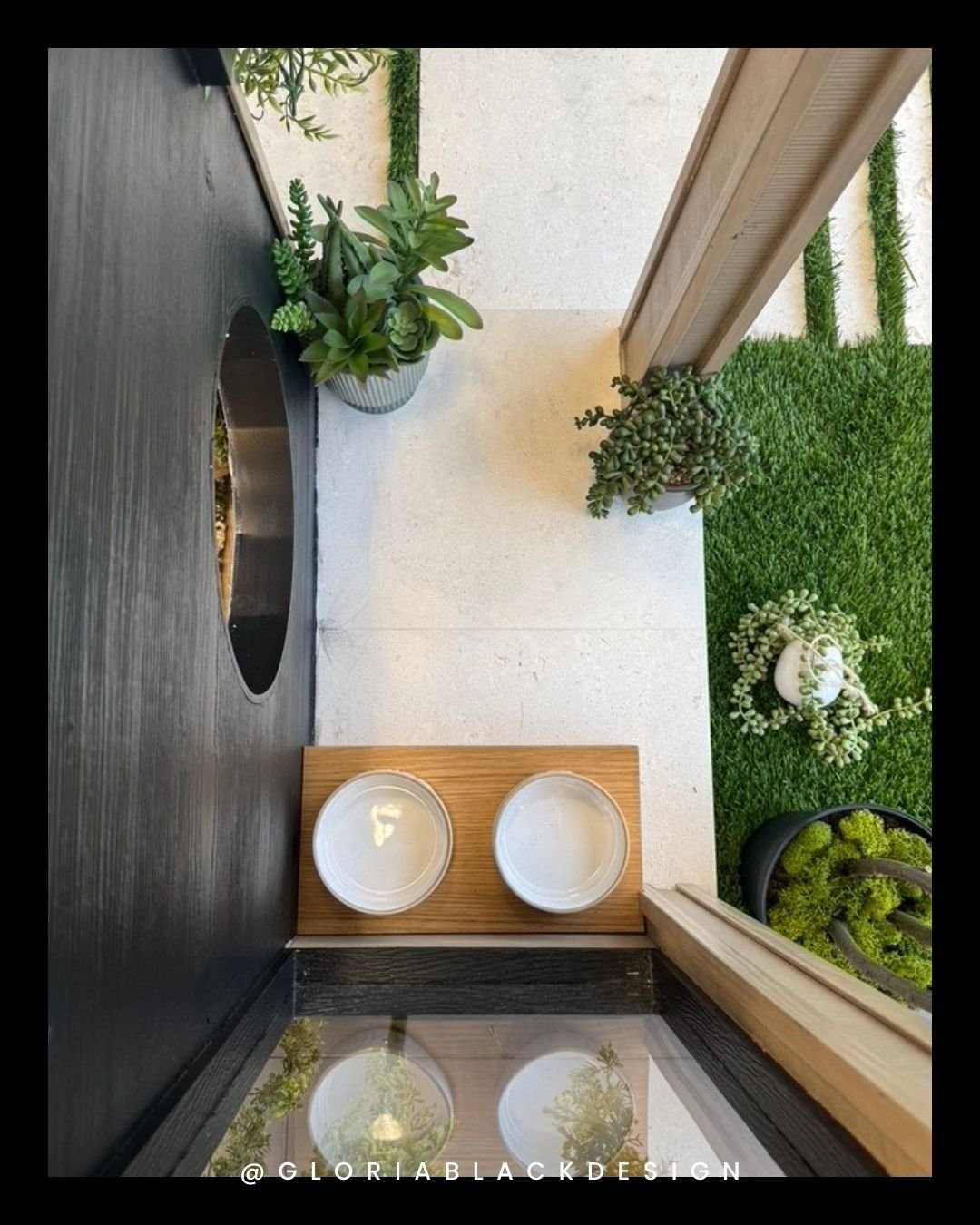 Top view of a modern garden patio with white tile flooring, green artificial grass, potted succulents, and two empty white bowls on a wooden stand. GLORIA BLACK DESIGN Great WOOF Lodge™ for SNIP Collier BARK & BUILD Ultimate Dog House Challenge