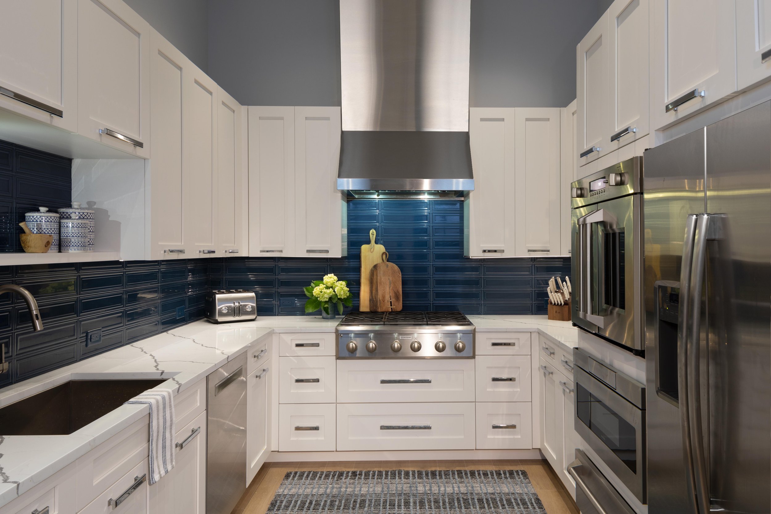 Modern butler's kitchen with white cabinets, stainless steel appliances, dark blue tile backsplash, and wooden cutting boards. Oven with French doors, blue rug, new build home in Talis Park Naples Florida, Palm Beach GLORIA BLACK