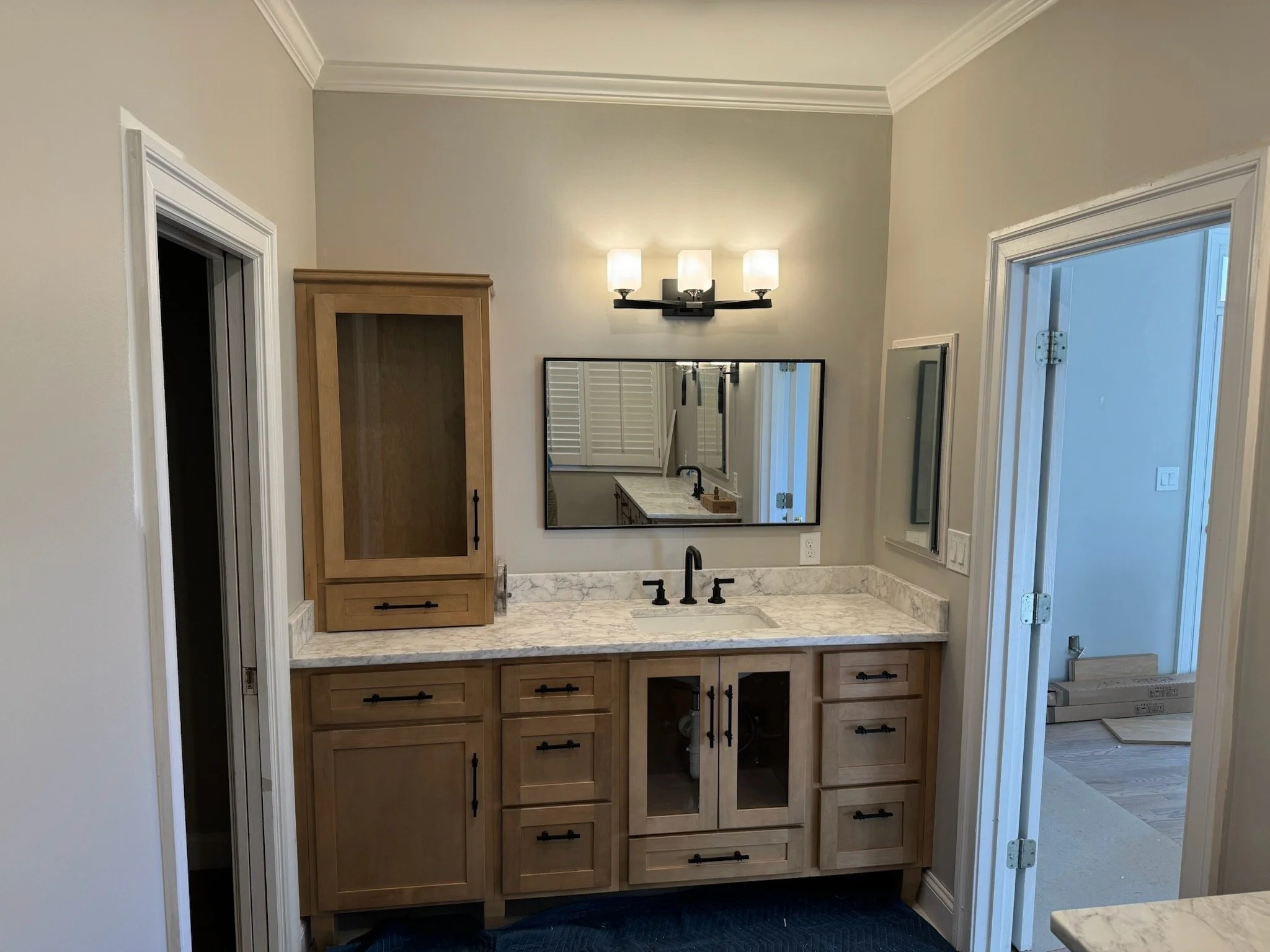A bathroom vanity with a butcher block countertop, black fixtures, and wooden cabinets, and a large mirror on the wall above the sink area.